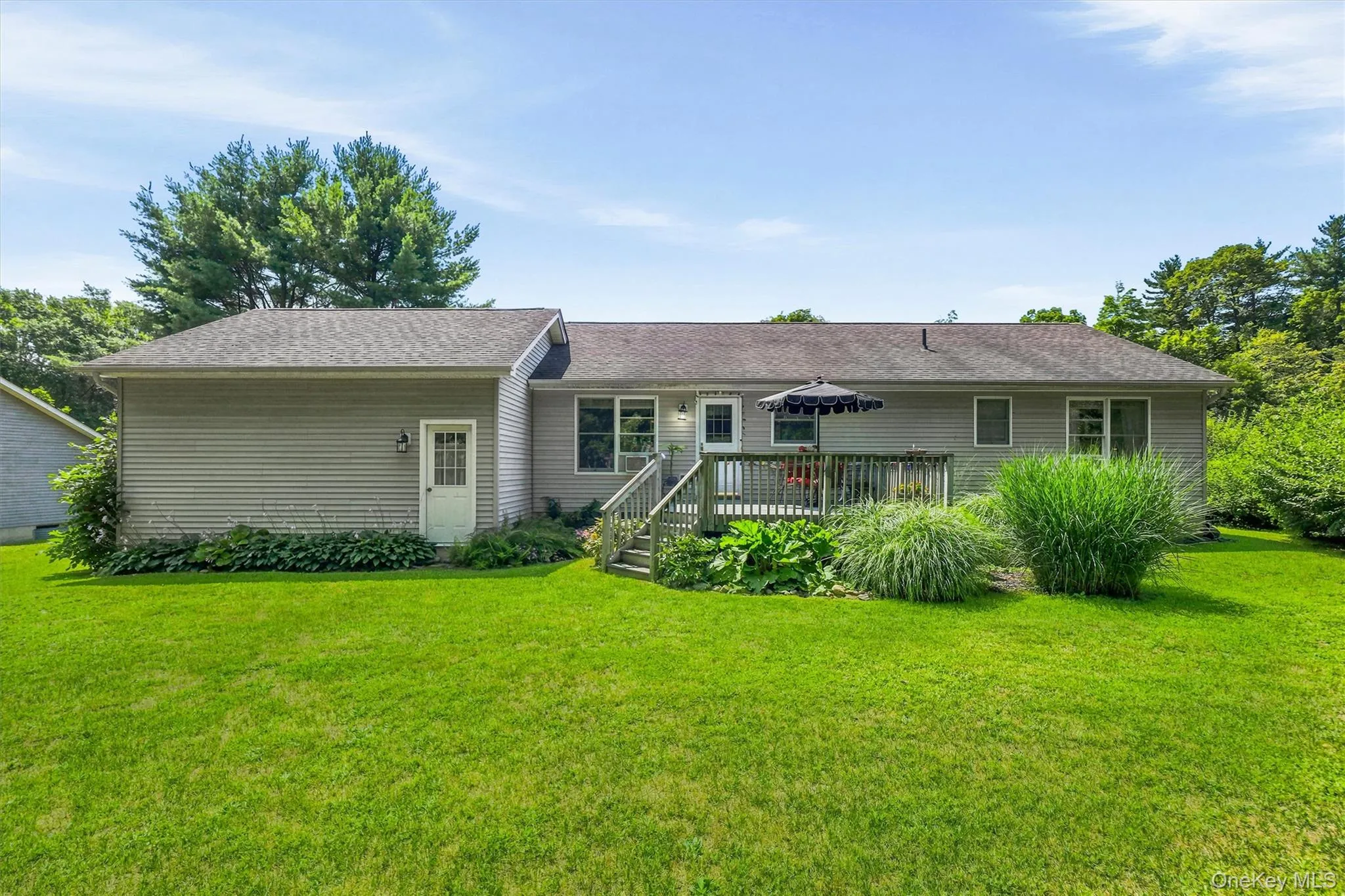 Expansive backyard featuring a large wooden deck with stairs, mature landscaping, and an external entry door Expansive backyard featuring a large wooden deck with stairs, mature landscaping, and an external entry door