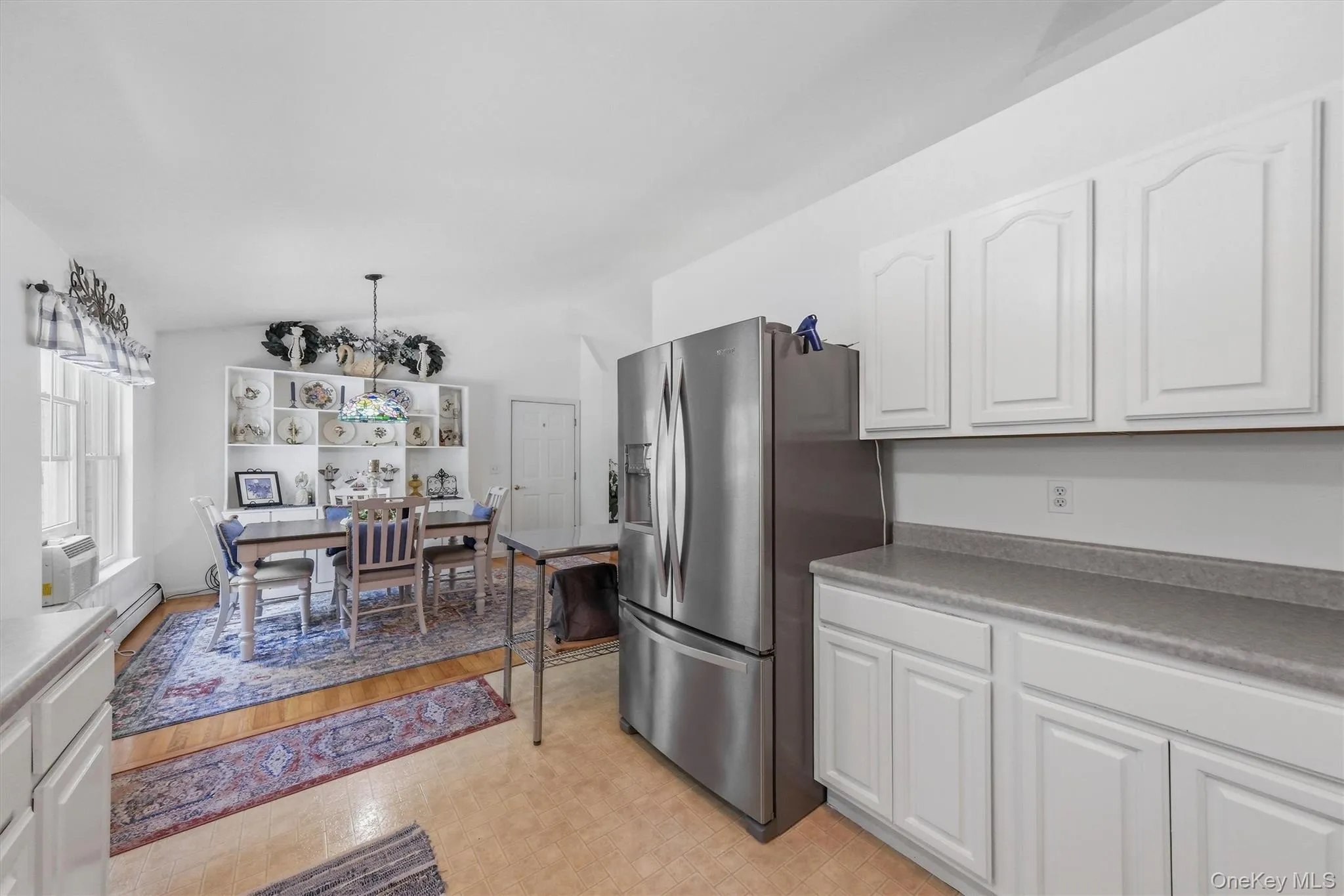 Open-concept space featuring wood-finish flooring, white cabinetry with light countertops, and an integrated stainless steel refrigerator Open-concept space featuring wood-finish flooring, white cabinetry with light countertops, and an integrated stainless steel refrigerator
