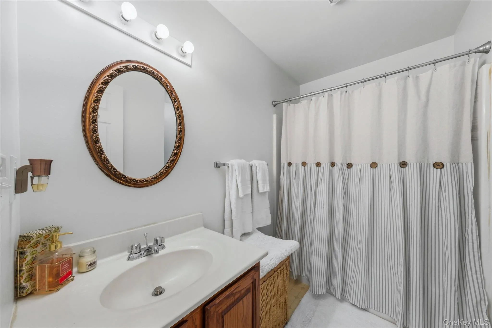 White vanity with an integrated sink, polished chrome faucet, wood-finish cabinetry, and an ornate round mirror White vanity with an integrated sink, polished chrome faucet, wood-finish cabinetry, and an ornate round mirror