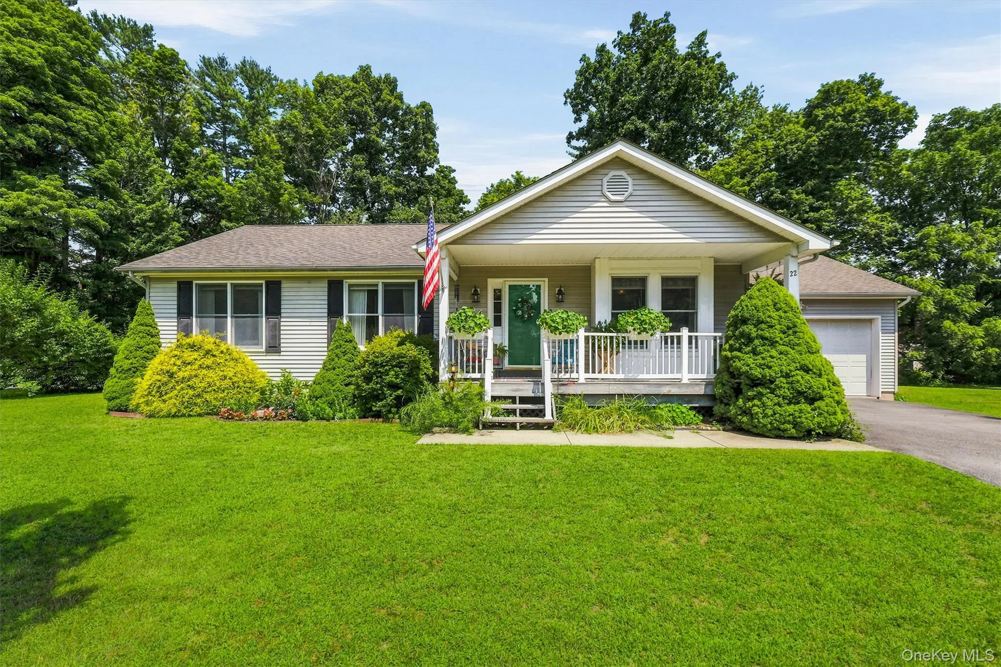 Ranch-style residence featuring light-colored siding, a covered front porch with white railings, a front-facing attached garage, and a lush green lawn Ranch-style residence featuring light-colored siding, a covered front porch with white railings, a front-facing attached garage, and a lush green lawn