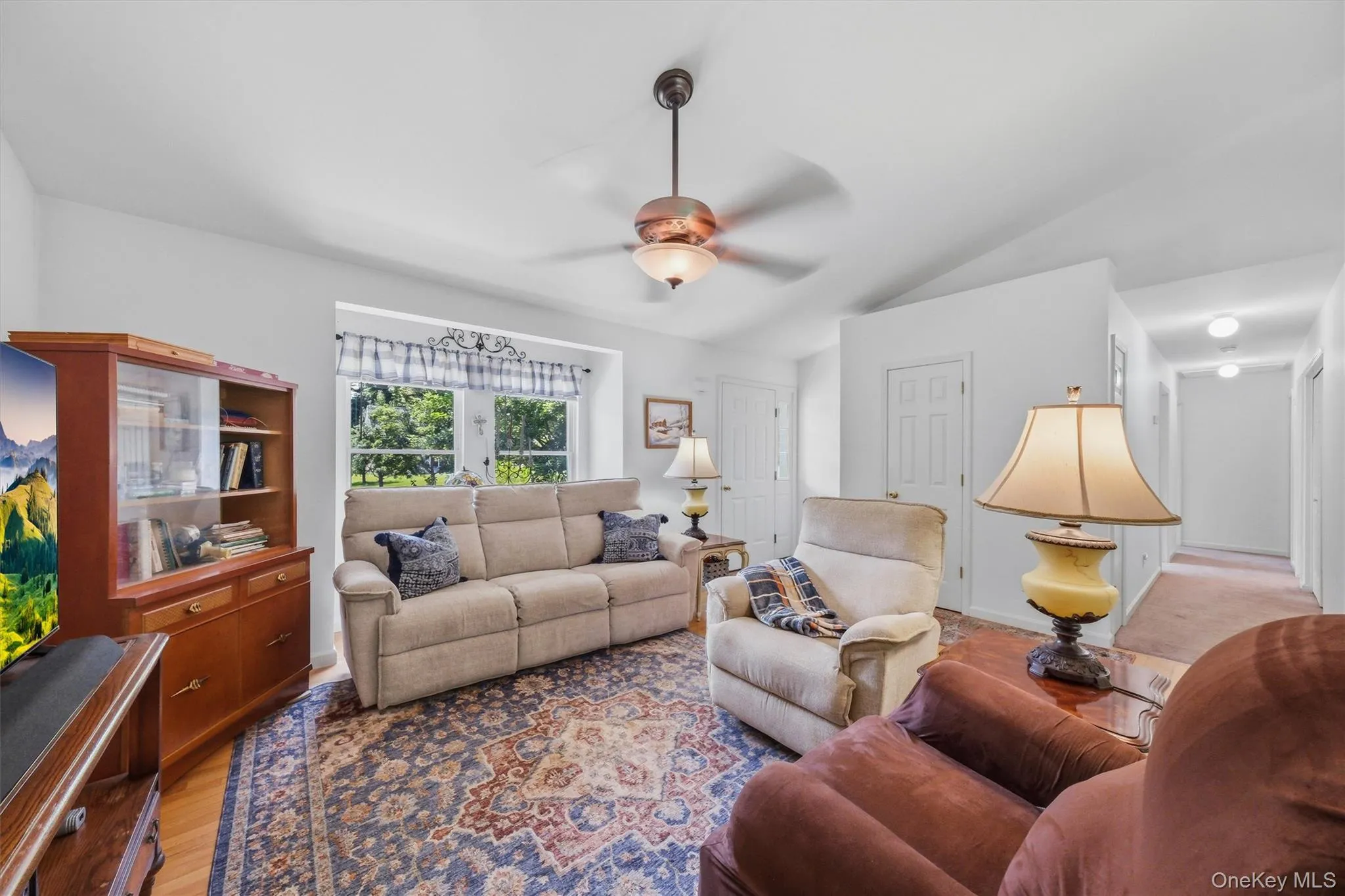 Vaulted ceiling with a ceiling fan, hardwood flooring, and a window with exterior tree views Vaulted ceiling with a ceiling fan, hardwood flooring, and a window with exterior tree views