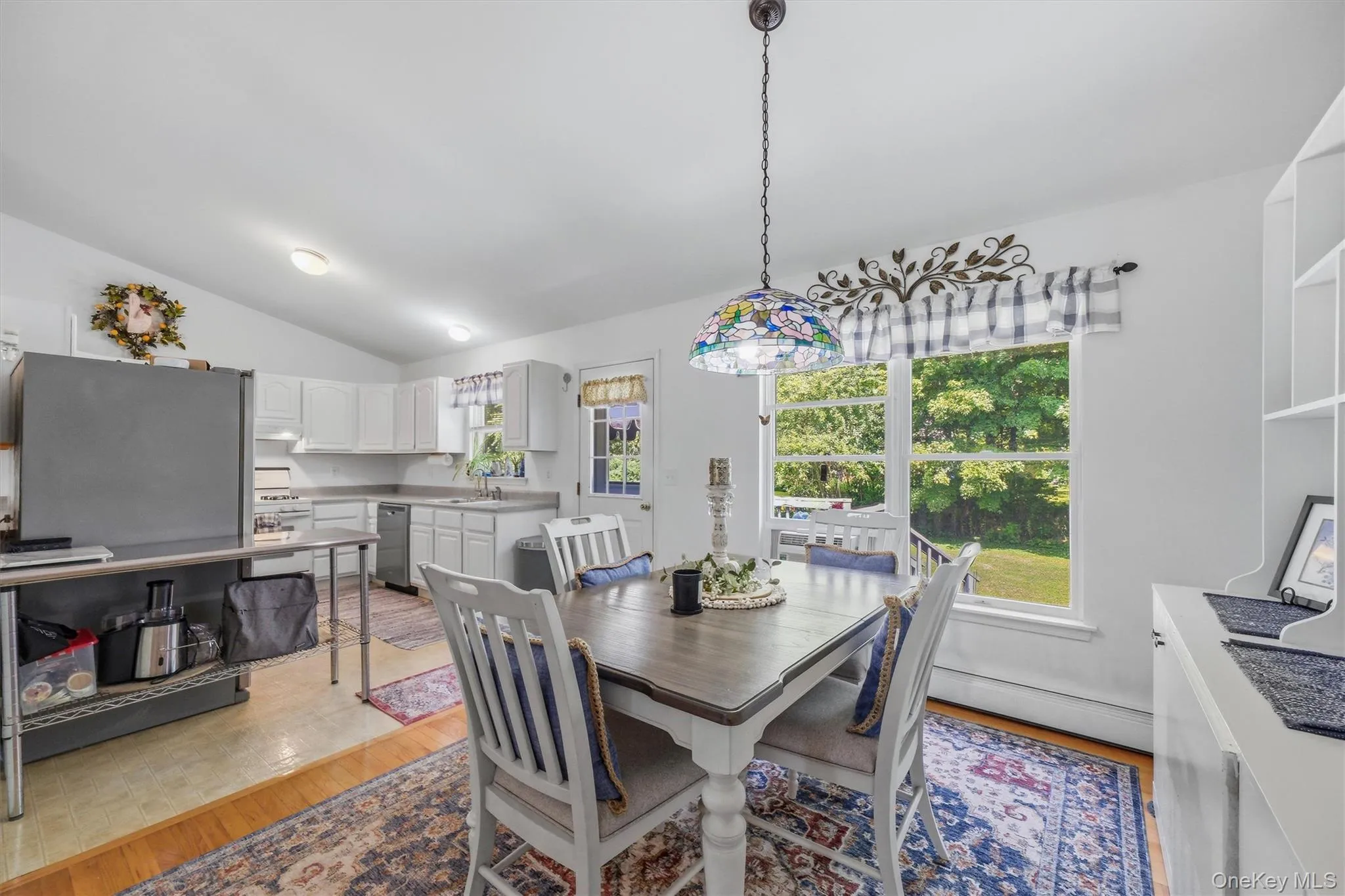 Vaulted ceilings, white kitchen cabinetry, stainless steel appliances, wood-finish flooring, and a decorative pendant light fixture Vaulted ceilings, white kitchen cabinetry, stainless steel appliances, wood-finish flooring, and a decorative pendant light fixture