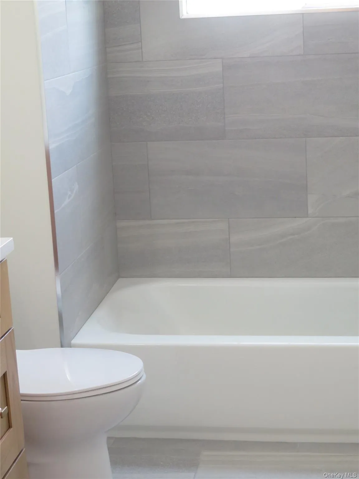 Bathroom featuring a white bathtub, light gray subway tile shower surround, and a white toilet Bathroom featuring a white bathtub, light gray subway tile shower surround, and a white toilet