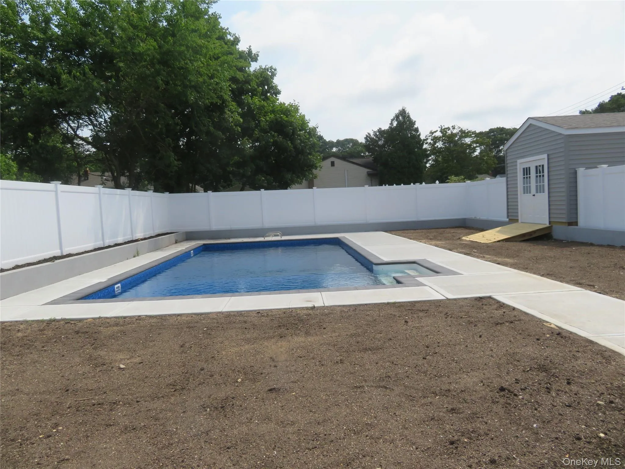 In-ground swimming pool with integrated steps, surrounded by concrete decking and a white vinyl privacy fence In-ground swimming pool with integrated steps, surrounded by concrete decking and a white vinyl privacy fence