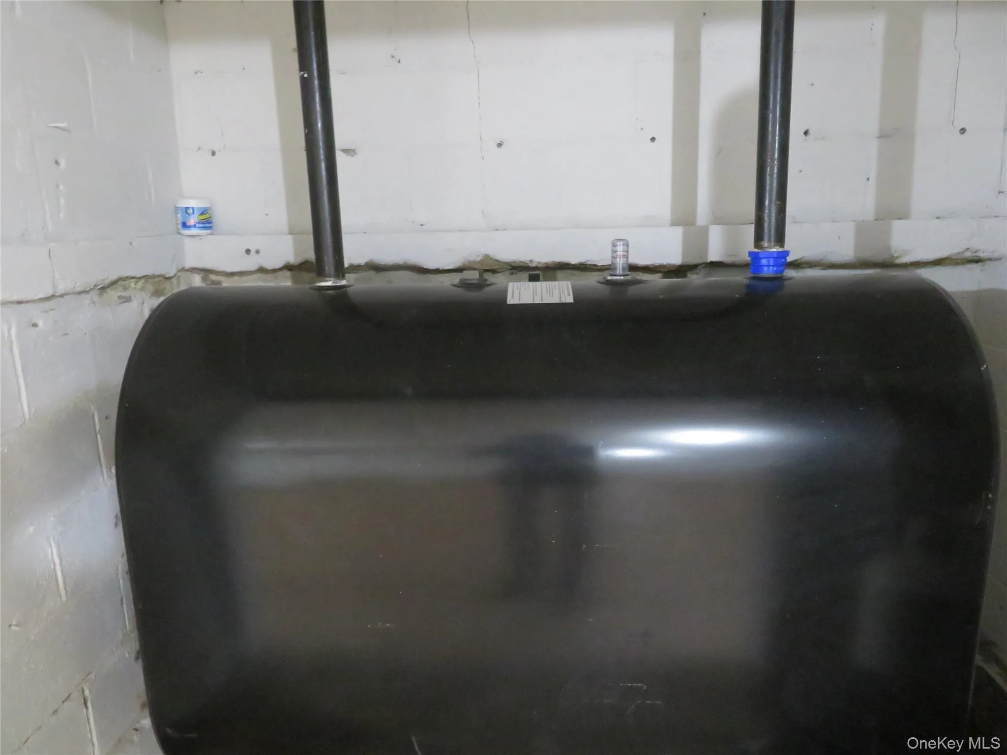 Black-painted oil tank with visible fill and vent pipes set against a white painted concrete block wall Black-painted oil tank with visible fill and vent pipes set against a white painted concrete block wall