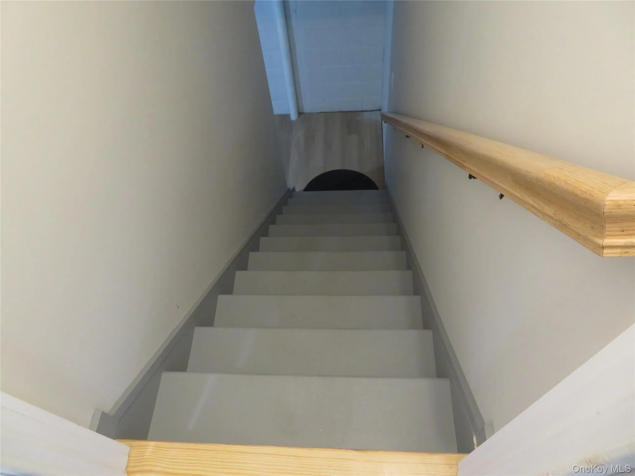 Stairwell featuring light gray treads, white risers, and a natural wood handrail leading to basement Stairwell featuring light gray treads, white risers, and a natural wood handrail leading to basement