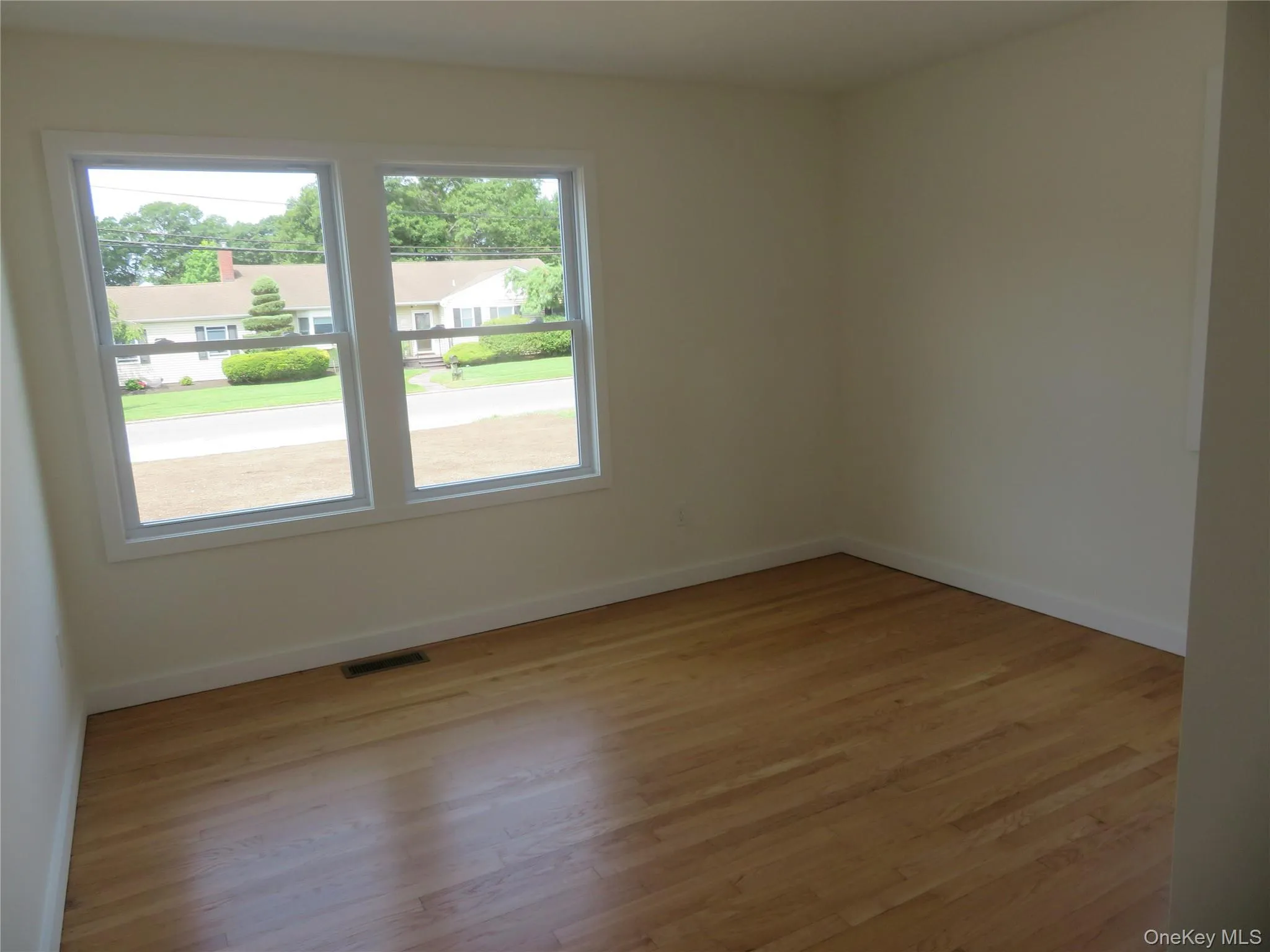Room featuring two large windows with white trim, wood-finish flooring, and light-toned walls Room featuring two large windows with white trim, wood-finish flooring, and light-toned walls