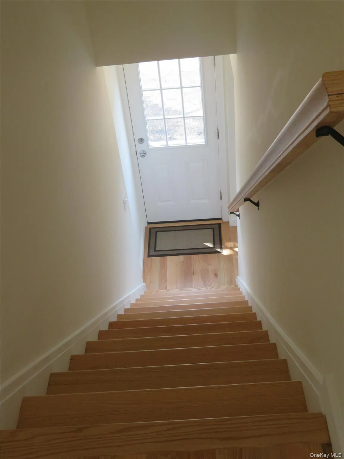 Natural wood-finish staircase with a coordinating wood handrail, leading to side door Natural wood-finish staircase with a coordinating wood handrail, leading to side door