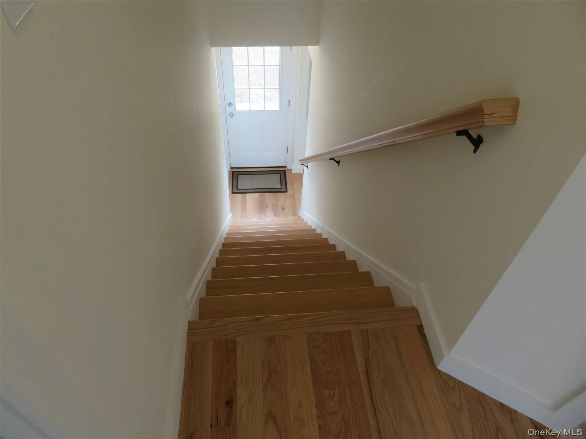 Hardwood staircase leading to 1st floor featuring natural wood treads and risers, a wood handrail with dark metal brackets, and light neutral wall paint Hardwood staircase leading to 1st floor featuring natural wood treads and risers, a wood handrail with dark metal brackets, and light neutral wall paint