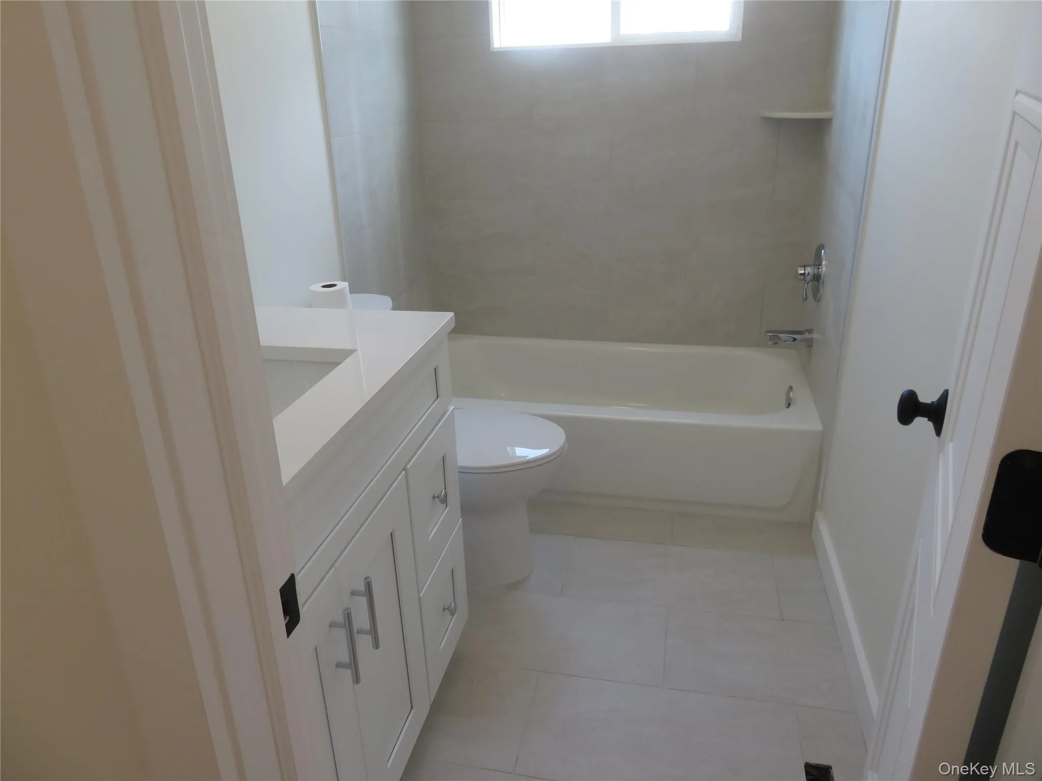 Modern bathroom featuring a white vanity with integrated sink, a white bathtub, and light-toned tile flooring Modern bathroom featuring a white vanity with integrated sink, a white bathtub, and light-toned tile flooring