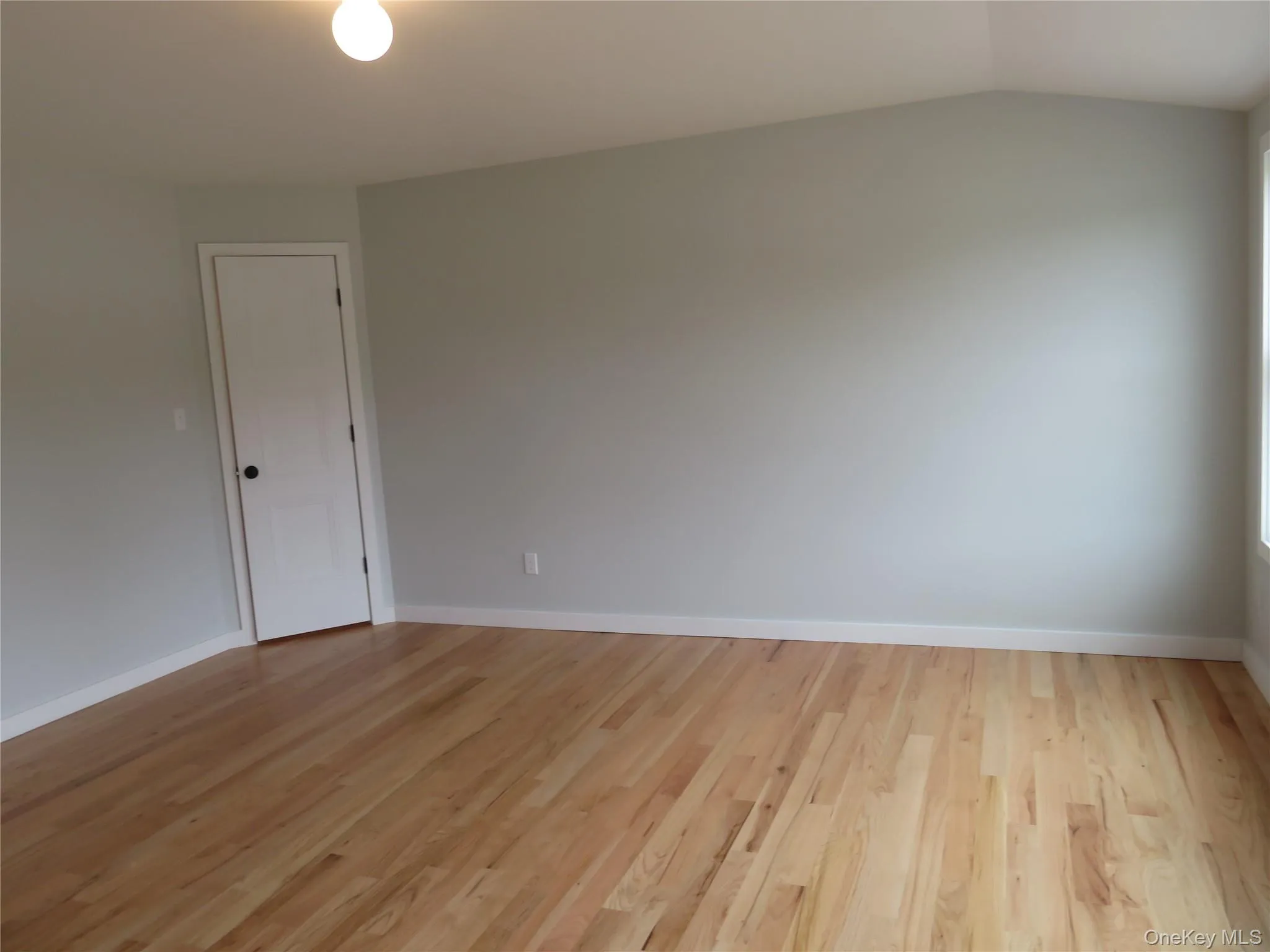 Master Bedroom. Spacious room featuring wood-finish flooring, light grey walls, white trim, and a vaulted ceiling with the shoes closet Master Bedroom. Spacious room featuring wood-finish flooring, light grey walls, white trim, and a vaulted ceiling with the shoes closet