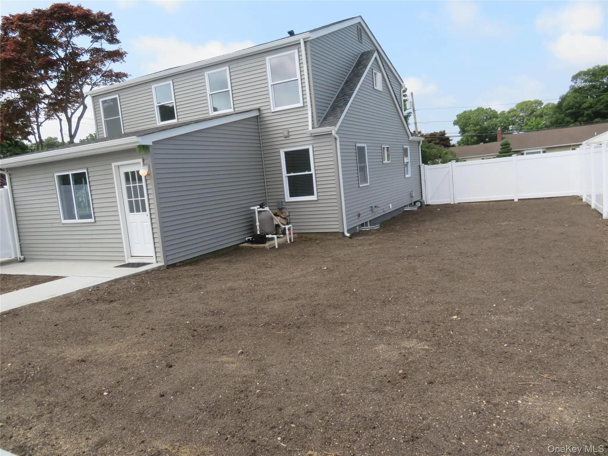 Exterior featuring gray siding, white trim windows, white privacy fencing, a concrete patio, and a newly prepared yard Exterior featuring gray siding, white trim windows, white privacy fencing, a concrete patio, and a newly prepared yard