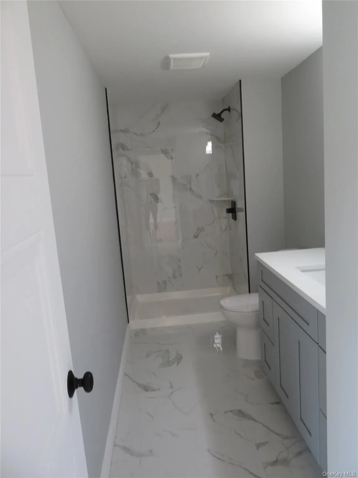 Master bath, A Modern bathroom featuring a walk-in shower with clear glass enclosure and black hardware, stone-finish tile shower surround, and a white shower pan Master bath, A Modern bathroom featuring a walk-in shower with clear glass enclosure and black hardware, stone-finish tile shower surround, and a white shower pan
