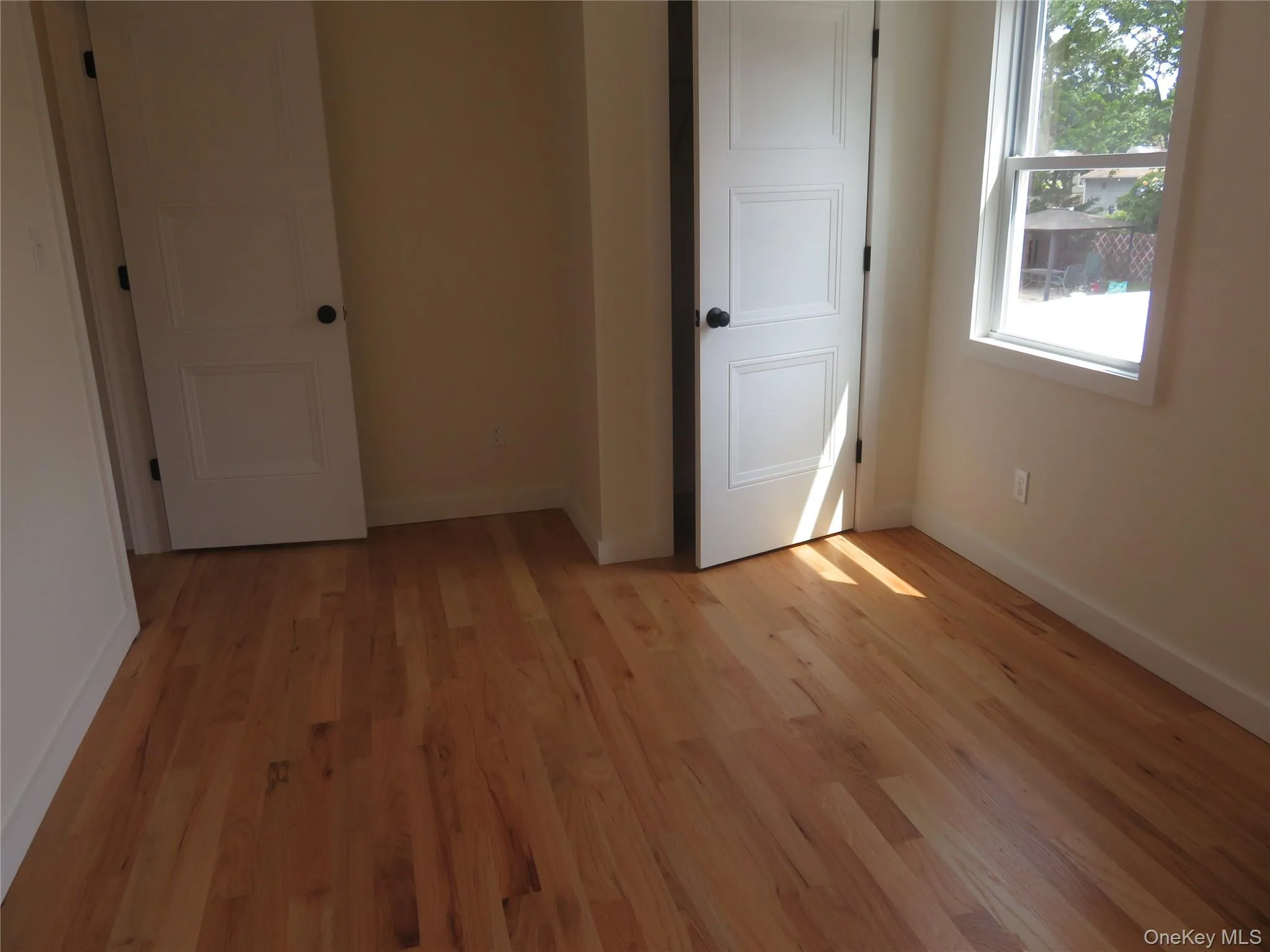Hardwood flooring throughout featuring painted baseboards, two paneled doors with black hardware, and a single-pane window with white trim Hardwood flooring throughout featuring painted baseboards, two paneled doors with black hardware, and a single-pane window with white trim