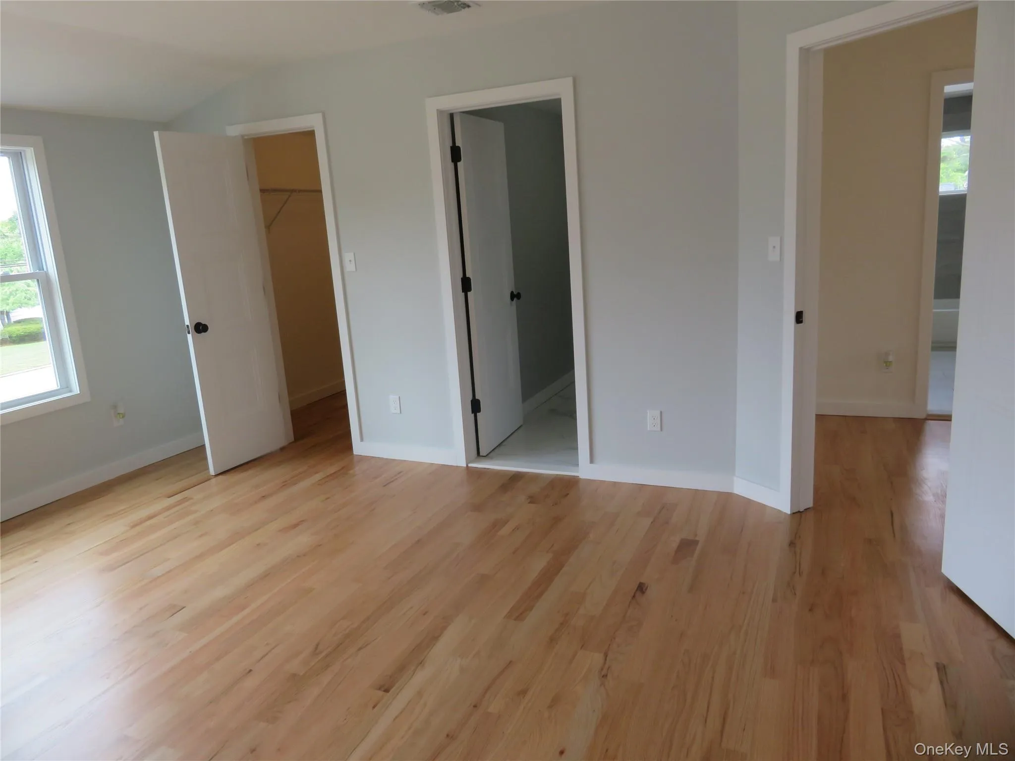 Master suite. Hardwood flooring throughout a room featuring a window with white trim, light-toned walls, and multiple doors to bath & walk in closet Master suite. Hardwood flooring throughout a room featuring a window with white trim, light-toned walls, and multiple doors to bath & walk in closet