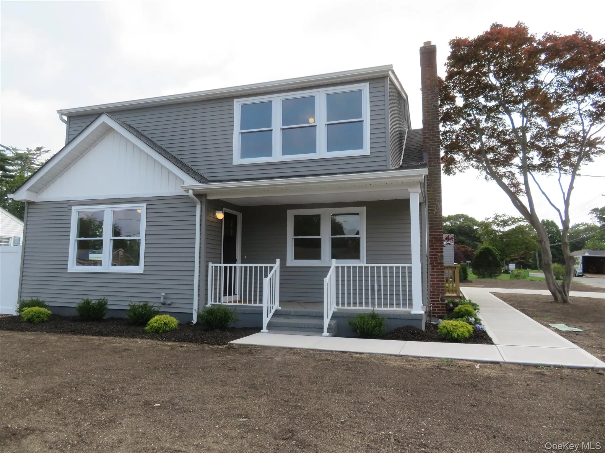 Gray siding exterior with white trim, featuring a covered front porch with white railings, a prominent brick chimney, and a concrete walkway Gray siding exterior with white trim, featuring a covered front porch with white railings, a prominent brick chimney, and a concrete walkway