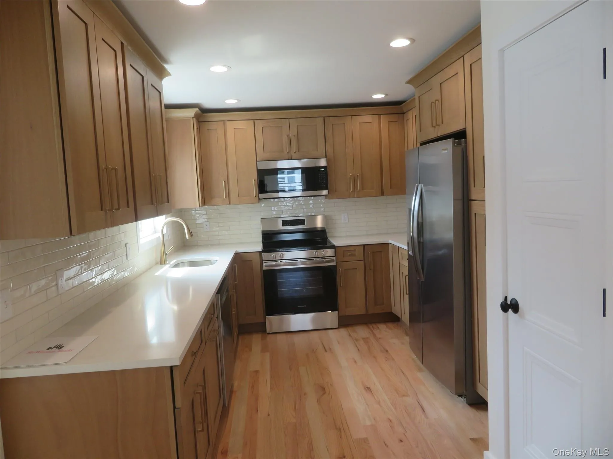 U-shaped kitchen featuring wood-finish cabinetry, light countertops, subway tile backsplash, and stainless steel appliances U-shaped kitchen featuring wood-finish cabinetry, light countertops, subway tile backsplash, and stainless steel appliances