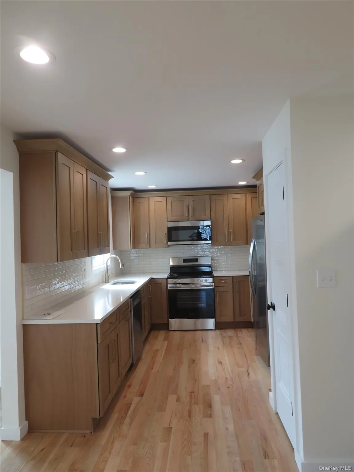 Kitchen featuring light wood-finish flooring, recessed lighting, and a white subway tile backsplash Kitchen featuring light wood-finish flooring, recessed lighting, and a white subway tile backsplash