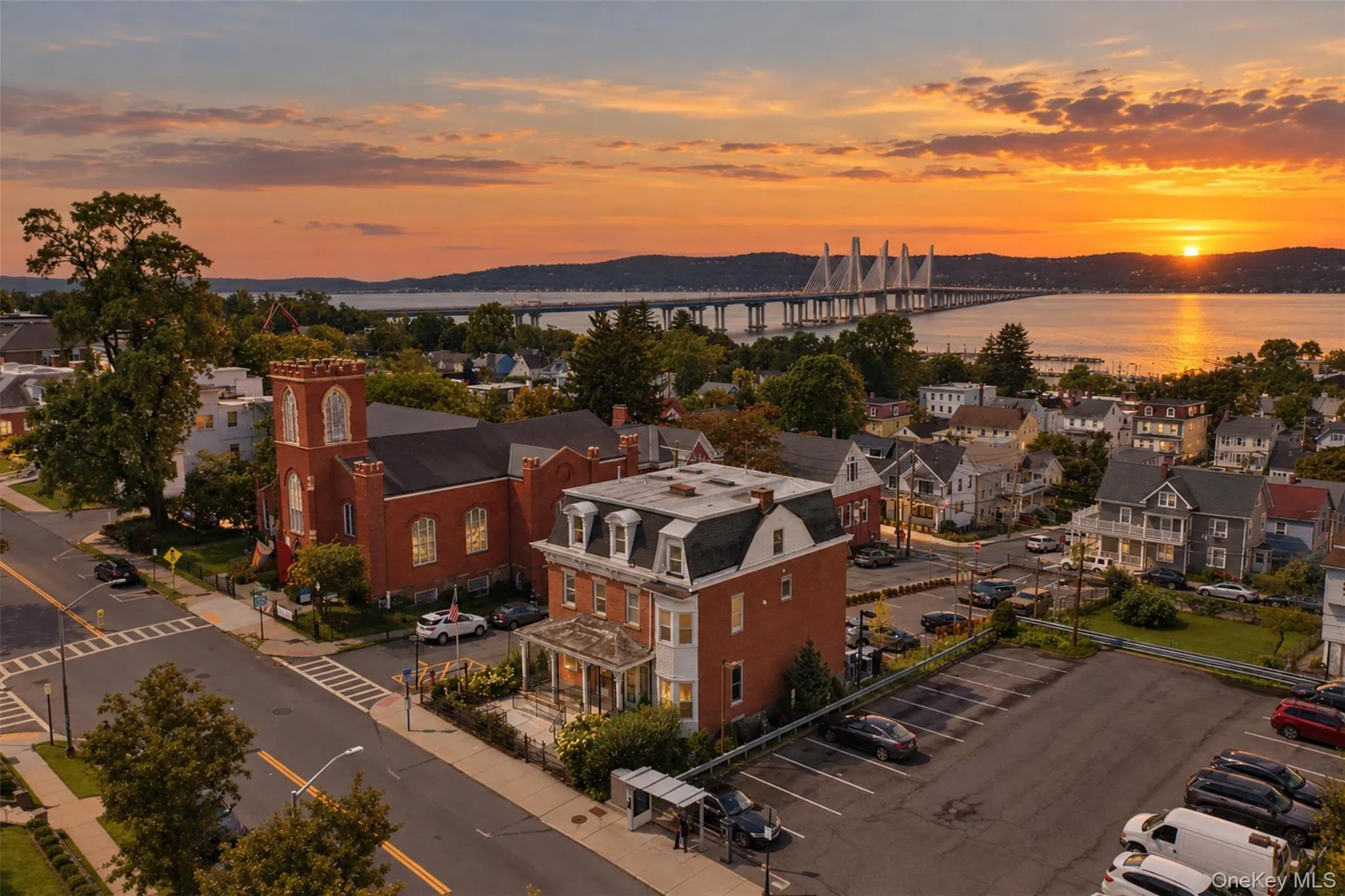 A breathtaking sunset aerial view captures the beauty and character of historic Tarrytown, with the property prominently positioned amid charming village architecture. Beyond the rooftops, the Hudson River glows in the evening light, while the Governor Mario M. Cuomo Bridge creates an iconic silhouette on the horizon. The image beautifully showcases the exceptional combination of historic charm, riverfront scenery, and a true Hudson Valley lifestyle A breathtaking sunset aerial view captures the beauty and character of historic Tarrytown, with the property prominently positioned amid charming village architecture. Beyond the rooftops, the Hudson River glows in the evening light, while the Governor Mario M. Cuomo Bridge creates an iconic silhouette on the horizon. The image beautifully showcases the exceptional combination of historic charm, riverfront scenery, and a true Hudson Valley lifestyle