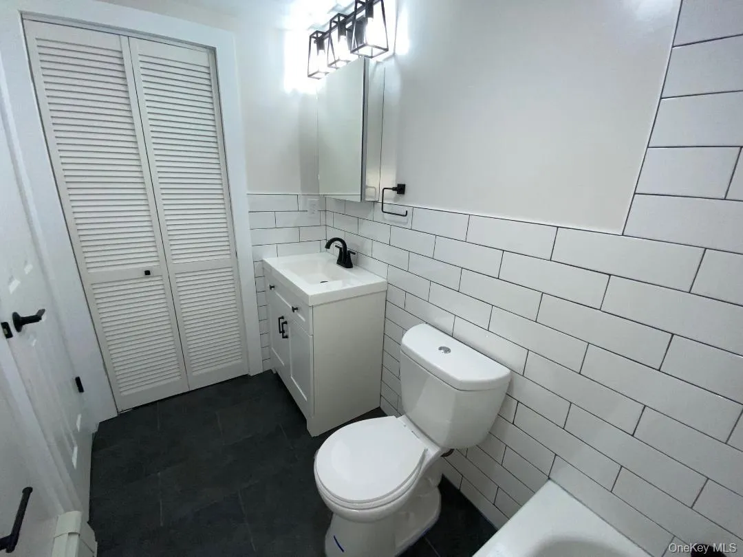 Bathroom featuring white subway tile walls, dark floor tiling, and a white vanity with a black faucet Bathroom featuring white subway tile walls, dark floor tiling, and a white vanity with a black faucet