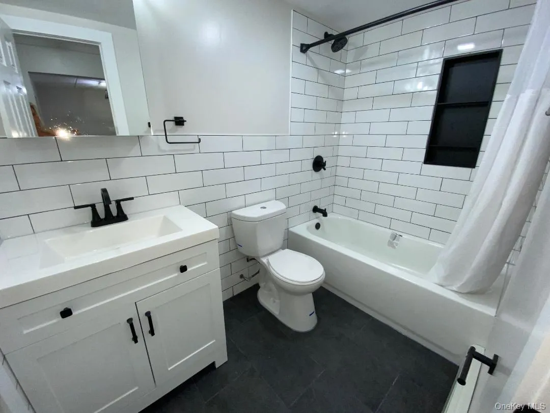 Beautifully updated bathroom featuring white subway tile surround, dark ceramic tile floor, white vanity with integrated sink, black matte fixtures, and a recessed shower niche Beautifully updated bathroom featuring white subway tile surround, dark ceramic tile floor, white vanity with integrated sink, black matte fixtures, and a recessed shower niche