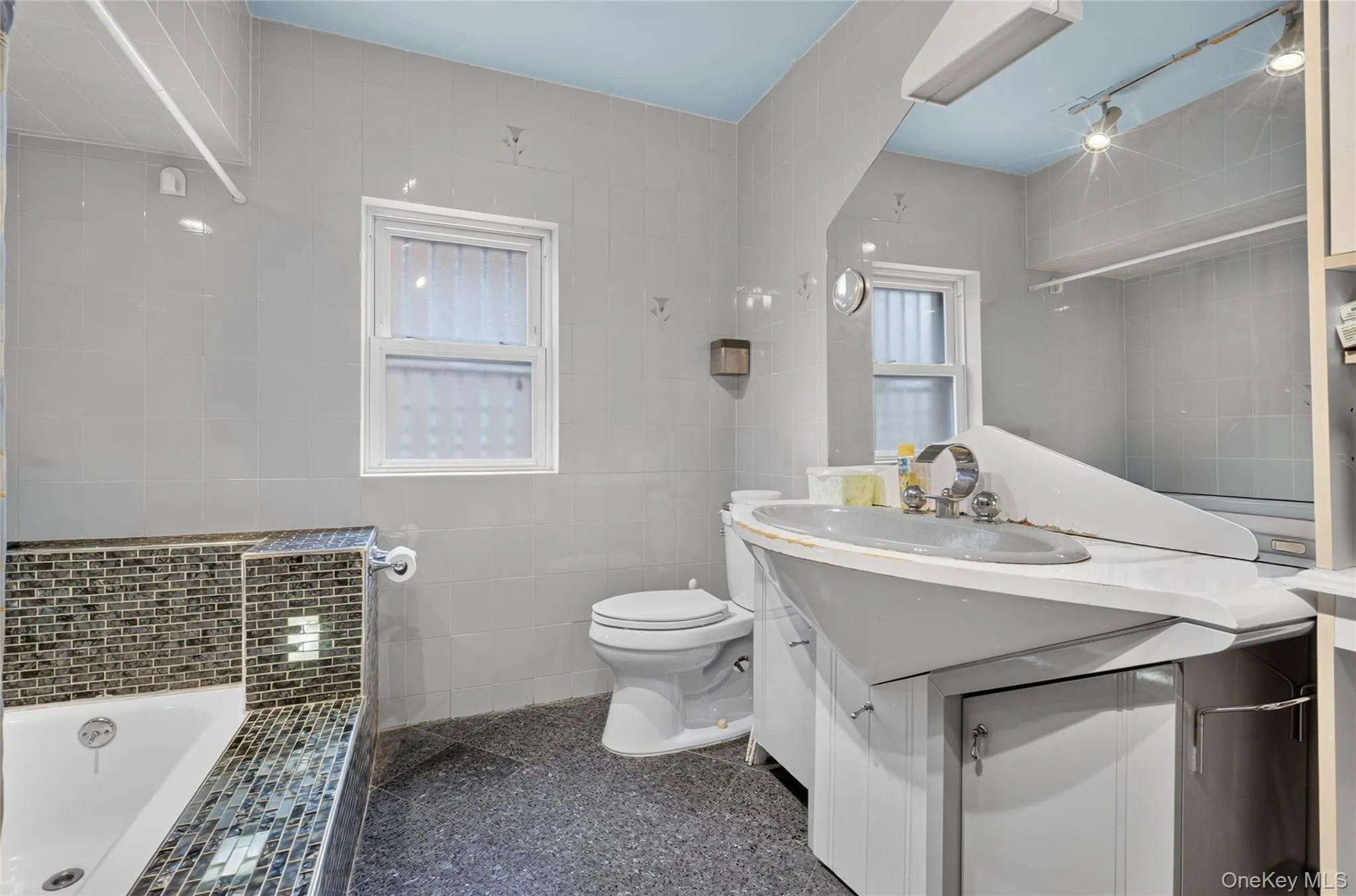 Bathroom featuring a built-in tub, mosaic tile accents, a vanity with an integrated sink, a toilet, and a window Bathroom featuring a built-in tub, mosaic tile accents, a vanity with an integrated sink, a toilet, and a window