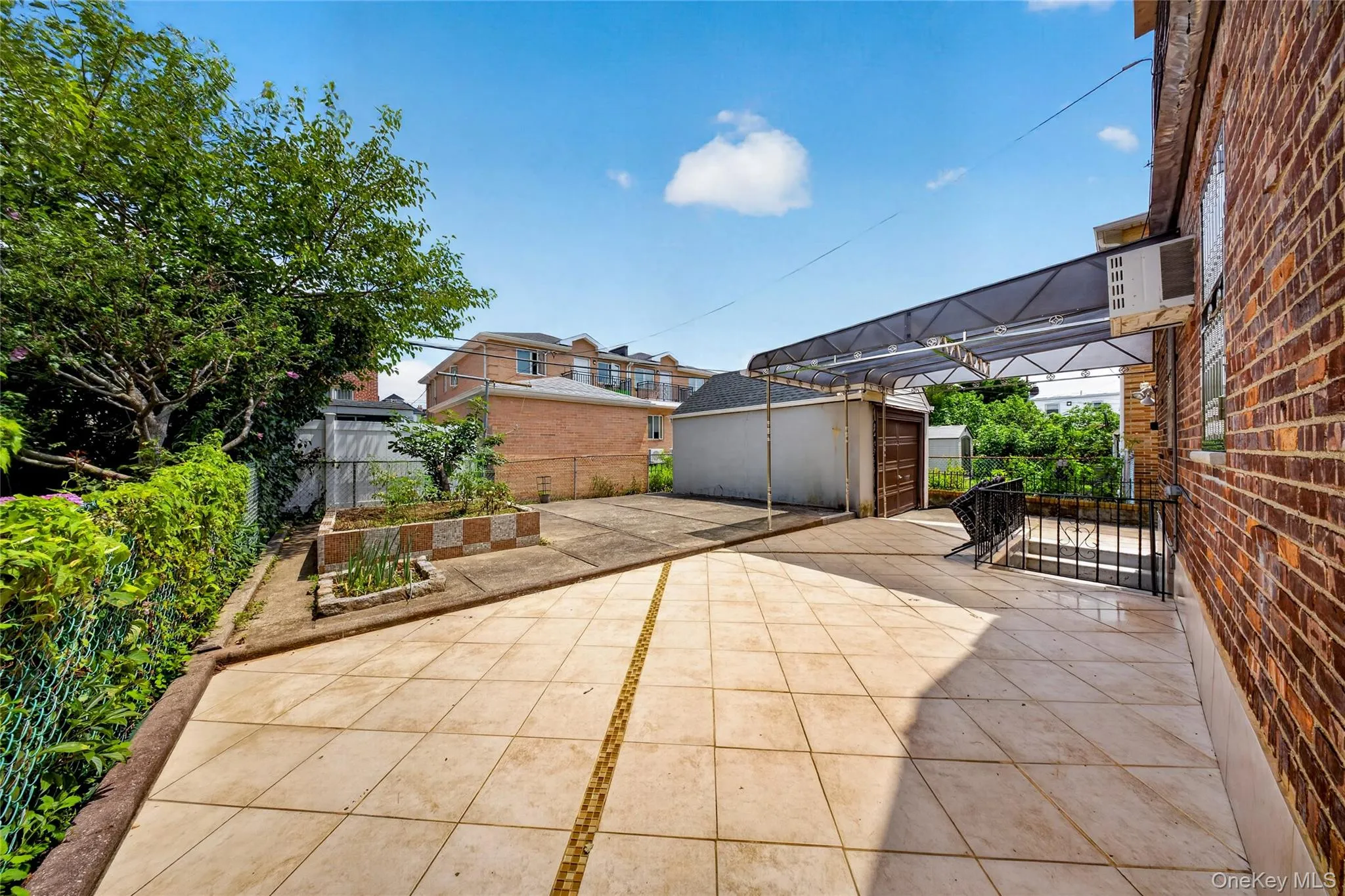 Paved patio area with light-colored tile flooring, featuring a large attached carport structure Paved patio area with light-colored tile flooring, featuring a large attached carport structure