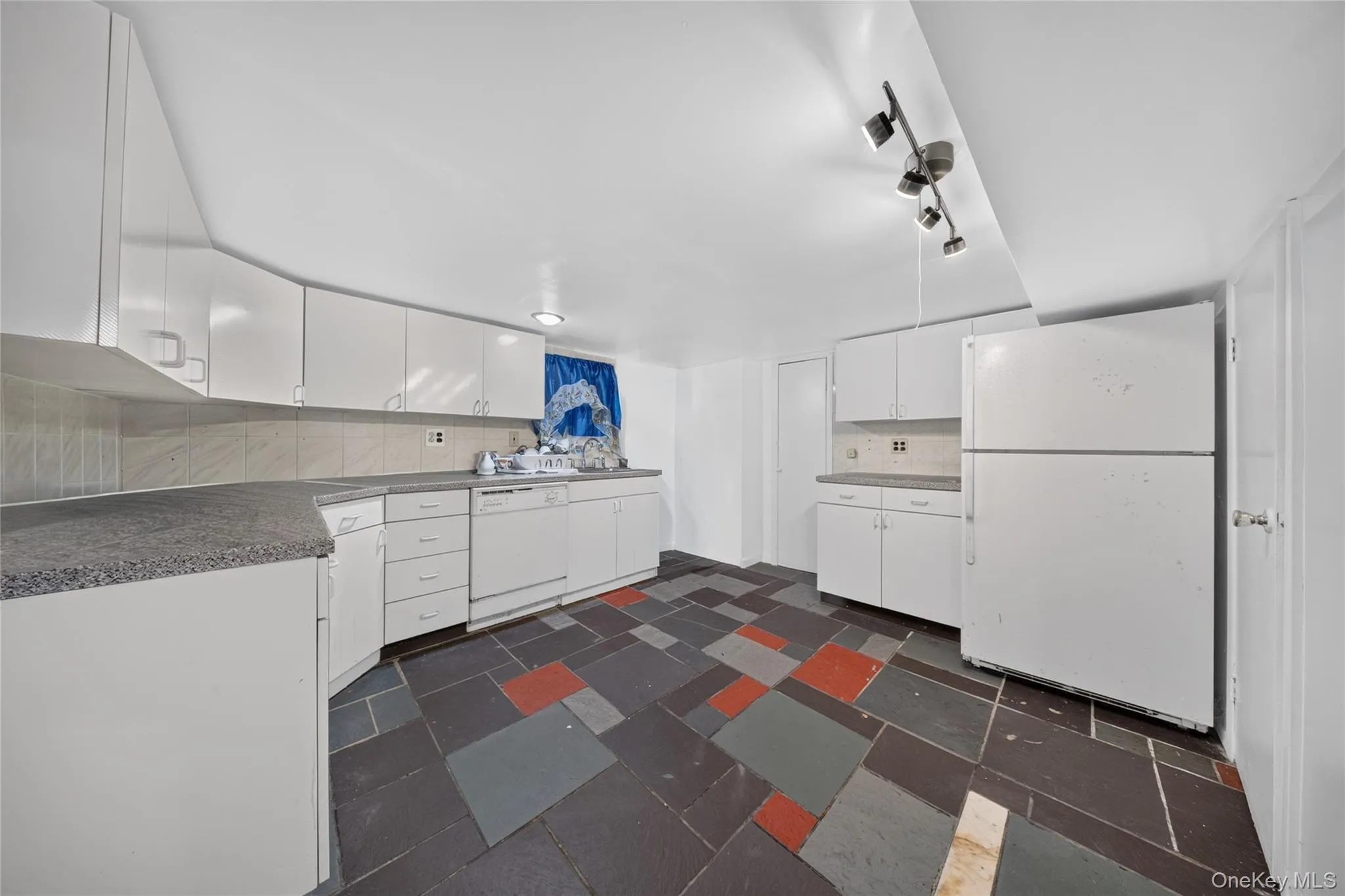 Kitchen featuring white cabinetry, gray speckled countertops, a built-in dishwasher, white refrigerator, and track lighting Kitchen featuring white cabinetry, gray speckled countertops, a built-in dishwasher, white refrigerator, and track lighting