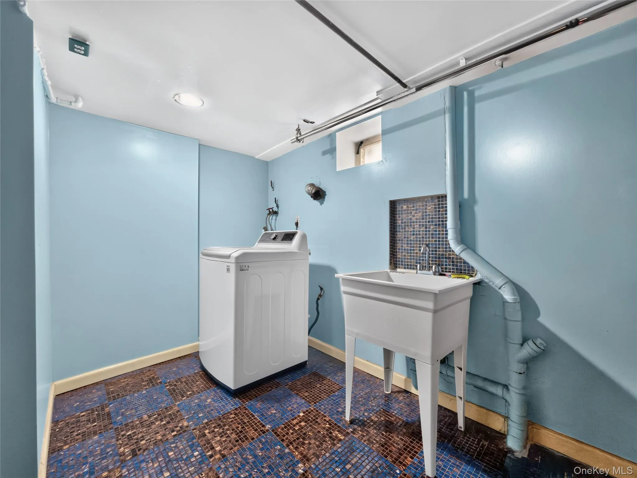 Dedicated laundry area featuring a utility sink with a tiled backsplash, overhead lighting, and checkerboard floor tiling Dedicated laundry area featuring a utility sink with a tiled backsplash, overhead lighting, and checkerboard floor tiling