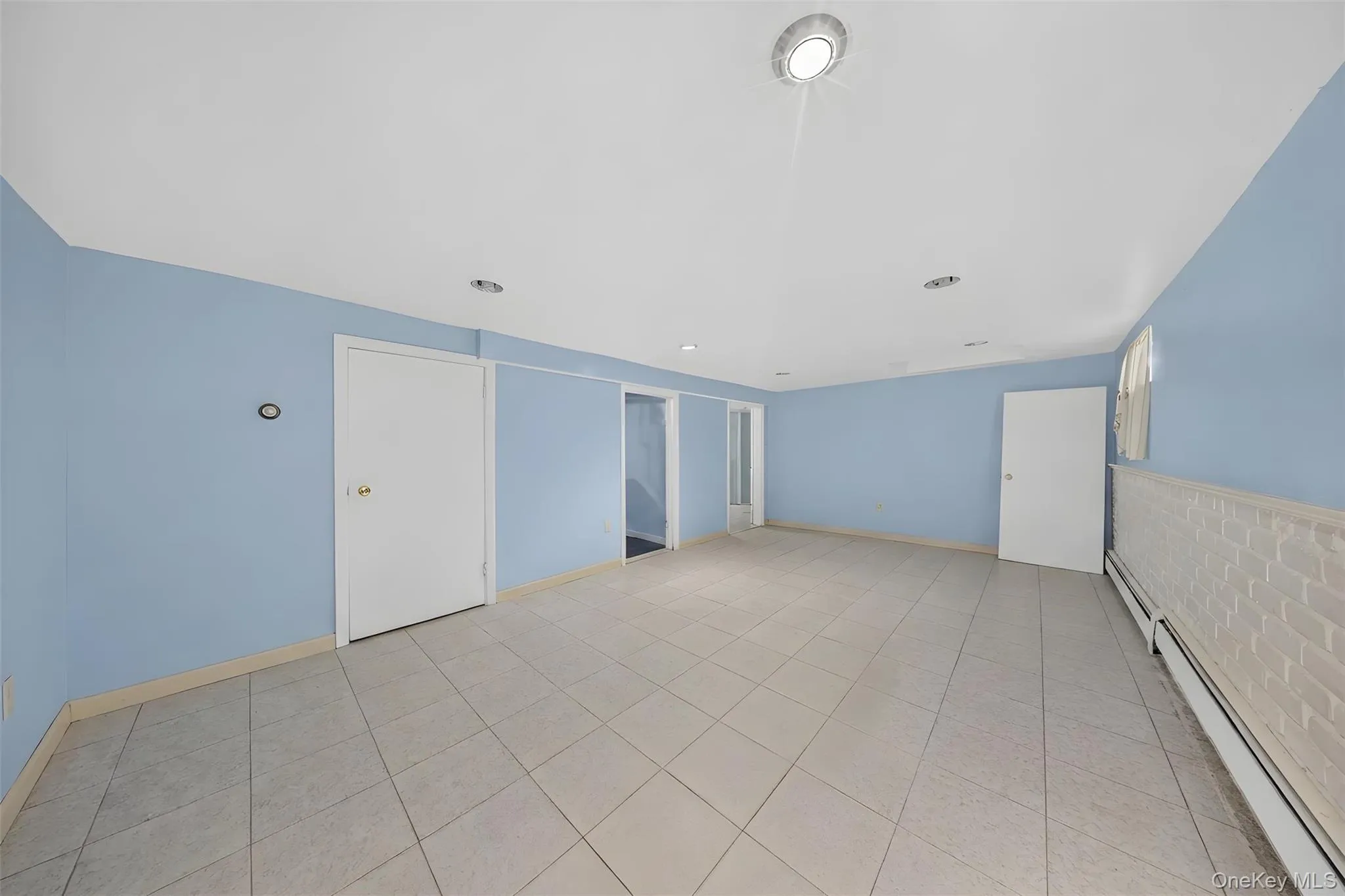 Spacious room featuring light blue walls, white trim, and light-toned tile flooring Spacious room featuring light blue walls, white trim, and light-toned tile flooring