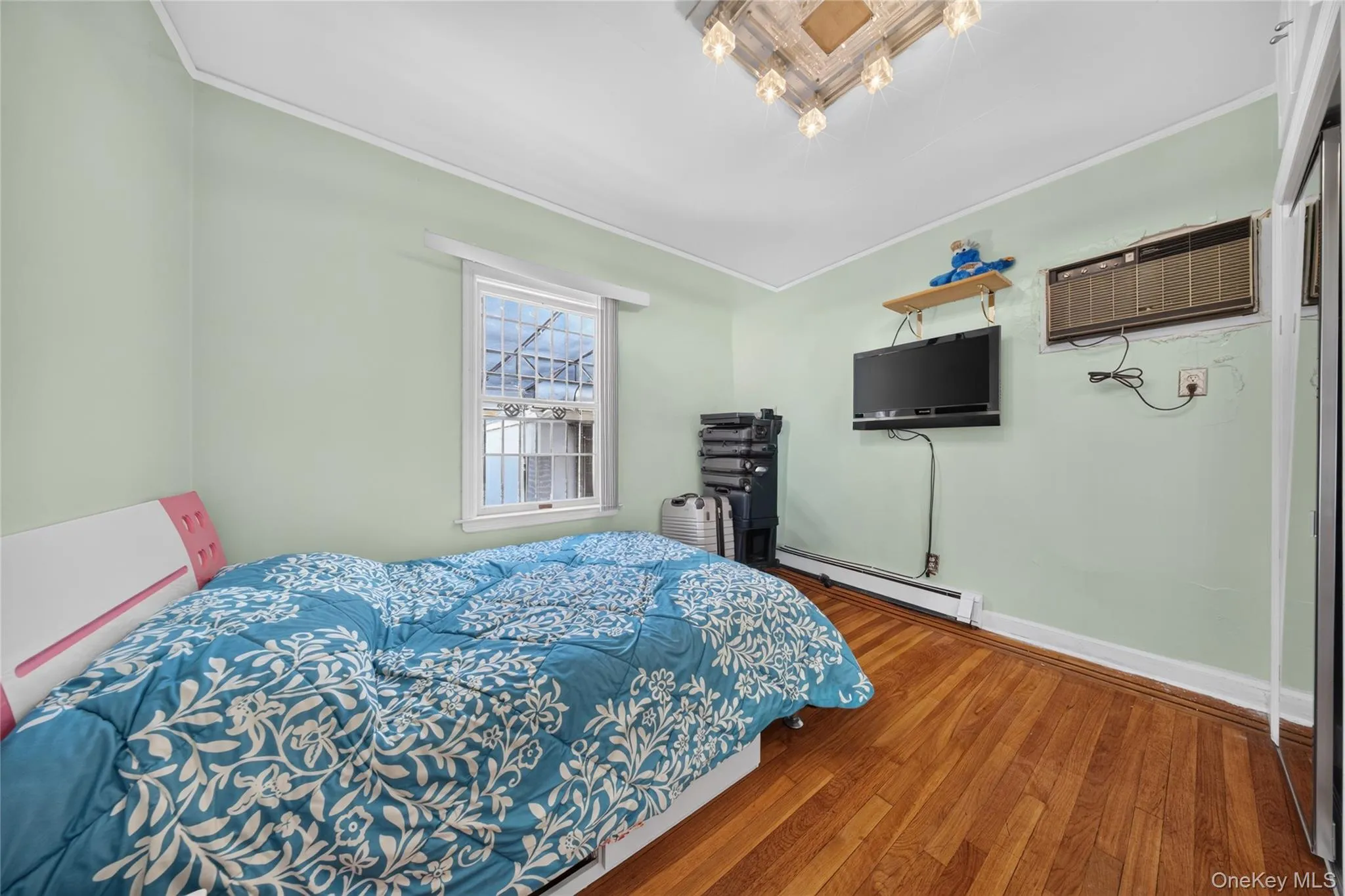 Room featuring wood-finish flooring, a window with exterior security bars, and light-colored wall paint Room featuring wood-finish flooring, a window with exterior security bars, and light-colored wall paint