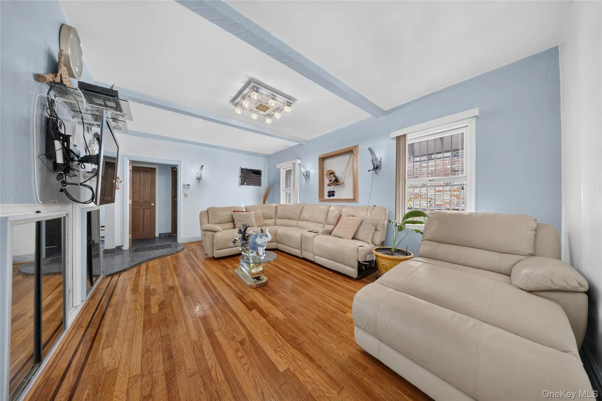 Bright living area featuring wood-finish flooring, light blue walls, and a recessed ceiling with decorative beams Bright living area featuring wood-finish flooring, light blue walls, and a recessed ceiling with decorative beams