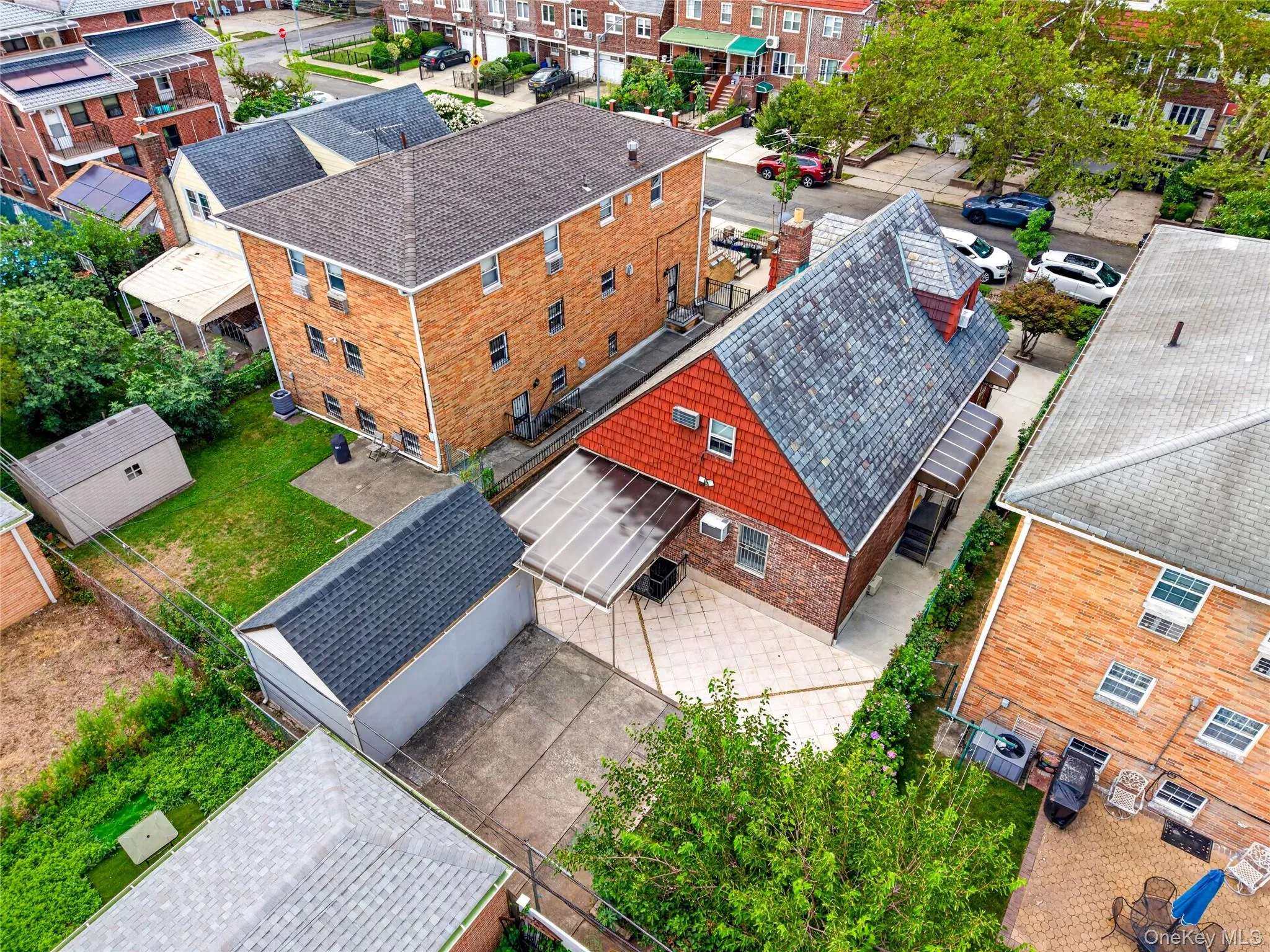 Residential property featuring a red shingle roof, brick exterior, and a paved patio area Residential property featuring a red shingle roof, brick exterior, and a paved patio area