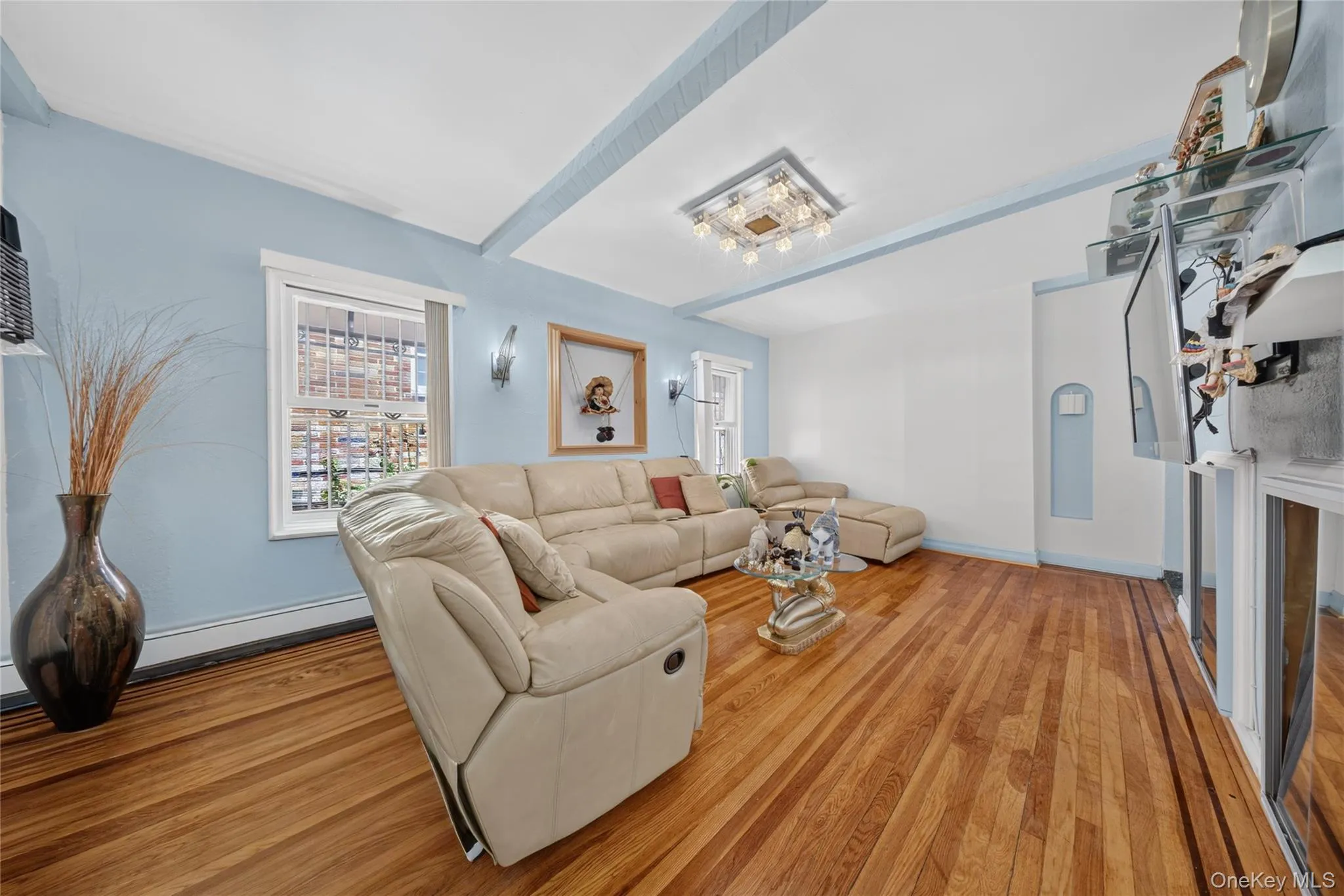 Living area featuring wood-finish flooring, light blue wall paint, and white ceiling beams Living area featuring wood-finish flooring, light blue wall paint, and white ceiling beams
