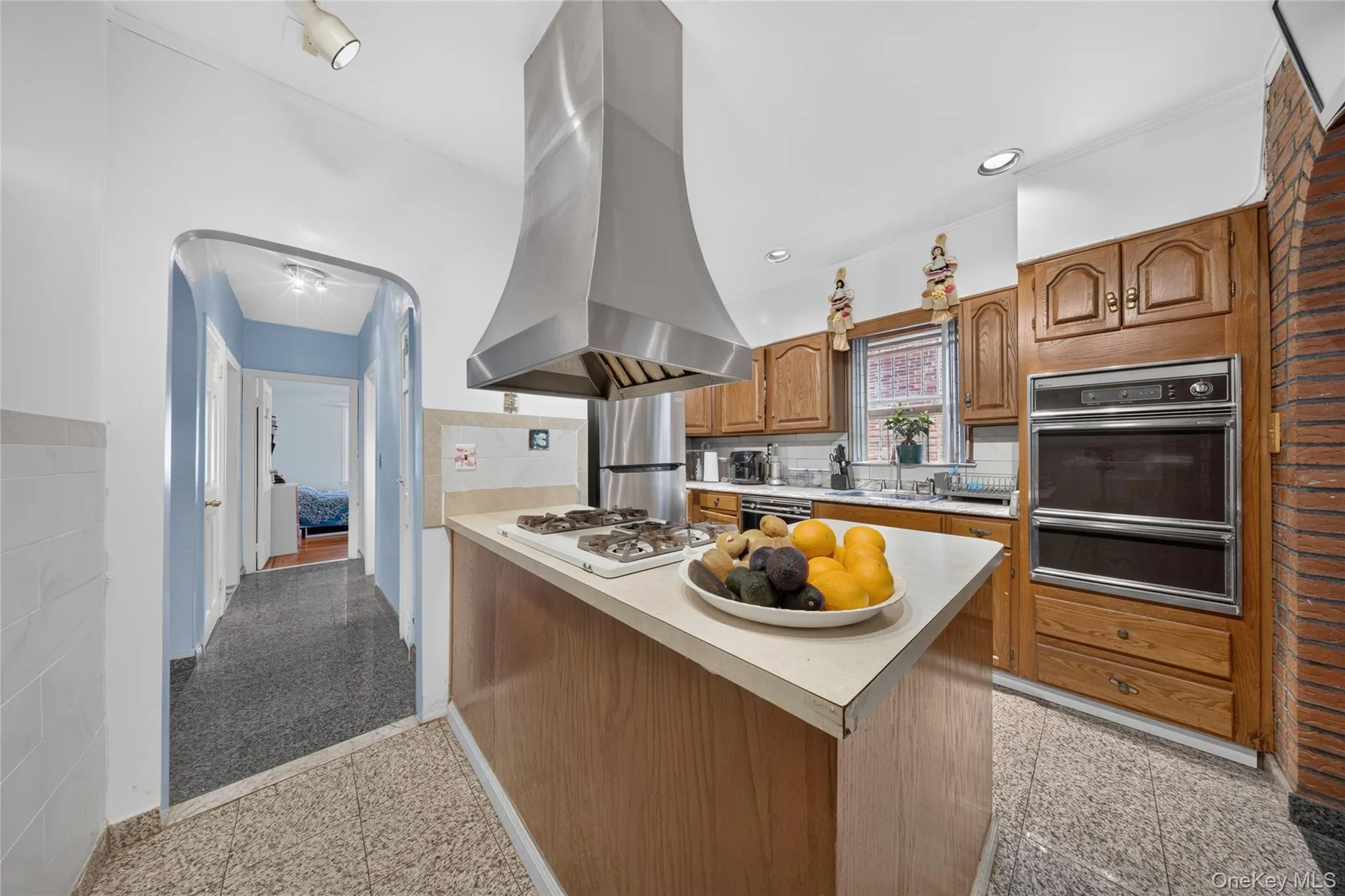 Kitchen featuring a stainless steel range hood, built-in double oven, wood-finish cabinetry, and a center island with a gas cooktop Kitchen featuring a stainless steel range hood, built-in double oven, wood-finish cabinetry, and a center island with a gas cooktop