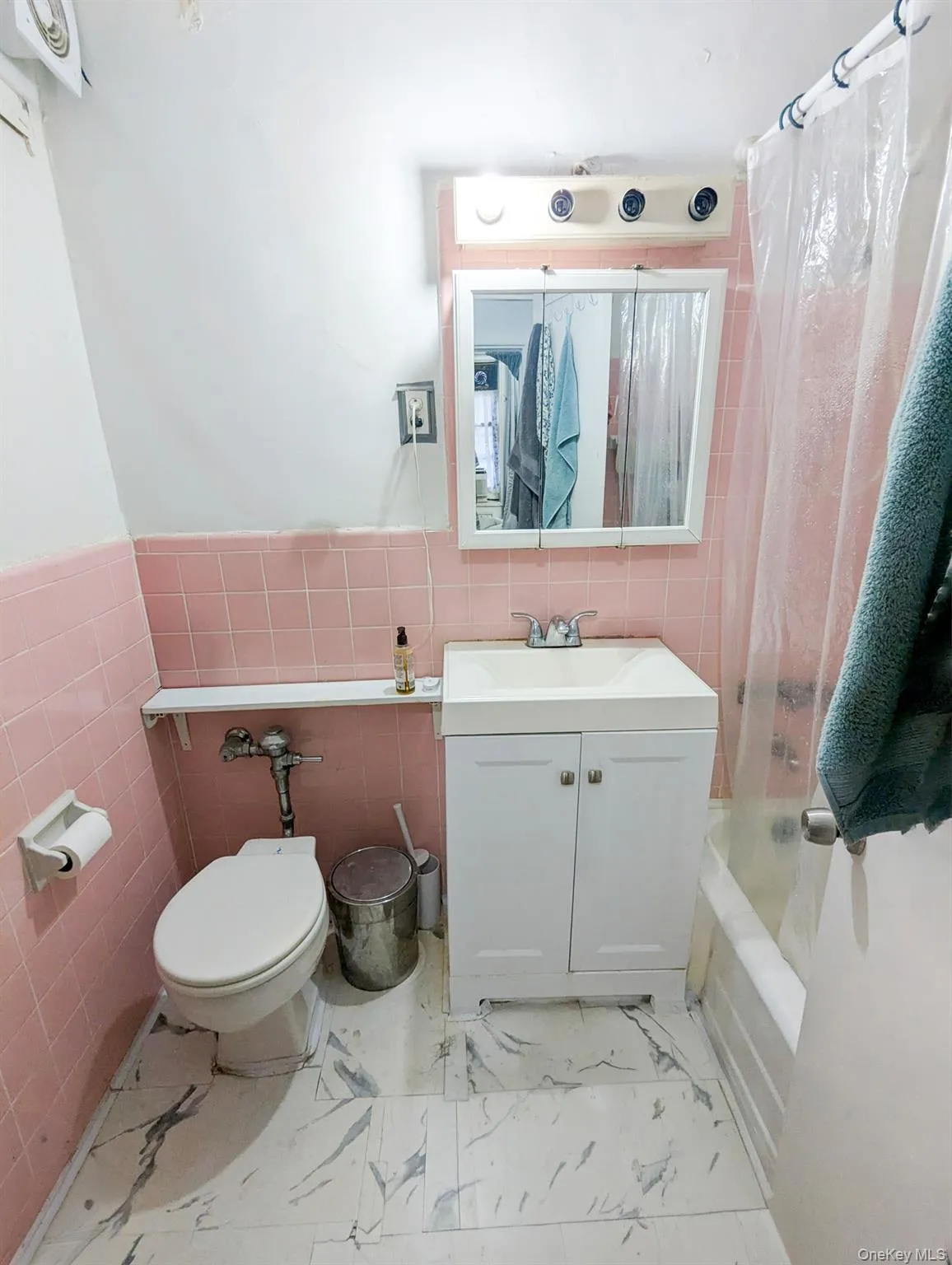Bathroom featuring pink wall tiling, white vanity with integrated sink, and a white tub. Bathroom featuring pink wall tiling, white vanity with integrated sink, and a white tub.