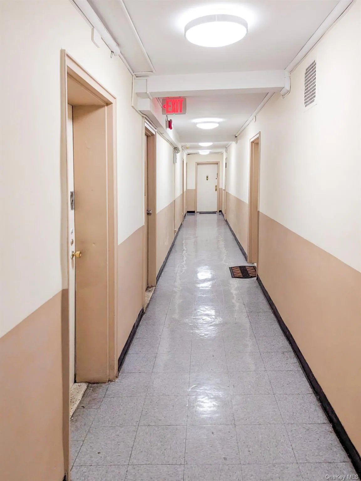Long hallway featuring a gray tiled floor, two-tone painted walls, and ceiling-mounted circular light fixtures Long hallway featuring a gray tiled floor, two-tone painted walls, and ceiling-mounted circular light fixtures