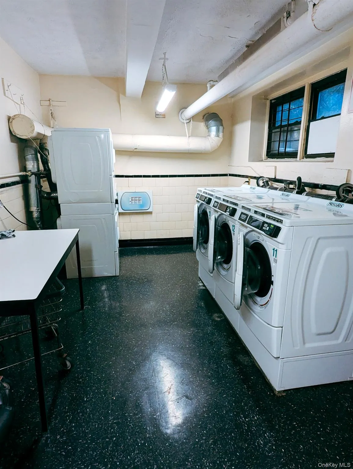 Dedicated laundry room featuring multiple front-load washing machines, a stacked washer/dryer unit, and a durable speckled flooring Dedicated laundry room featuring multiple front-load washing machines, a stacked washer/dryer unit, and a durable speckled flooring