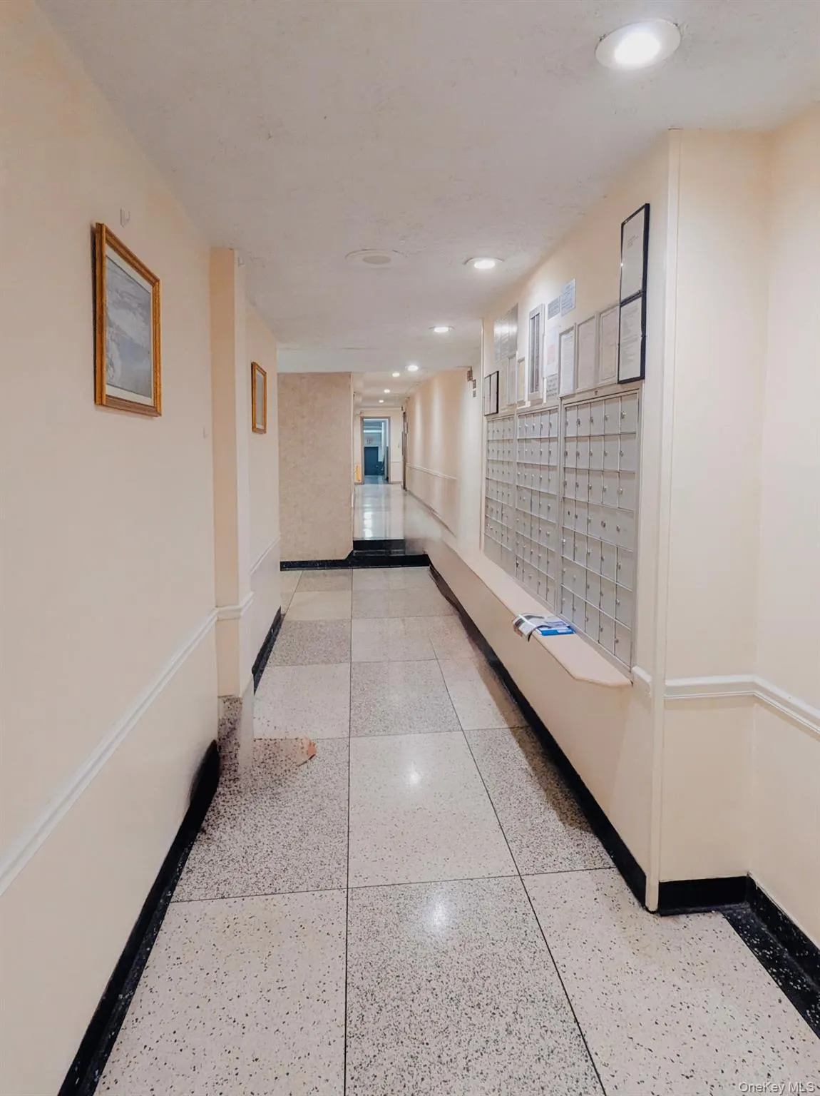 Building entryway featuring recessed lighting, a built-in mail system, speckled floor tiles, and a contrasting black baseboard Building entryway featuring recessed lighting, a built-in mail system, speckled floor tiles, and a contrasting black baseboard