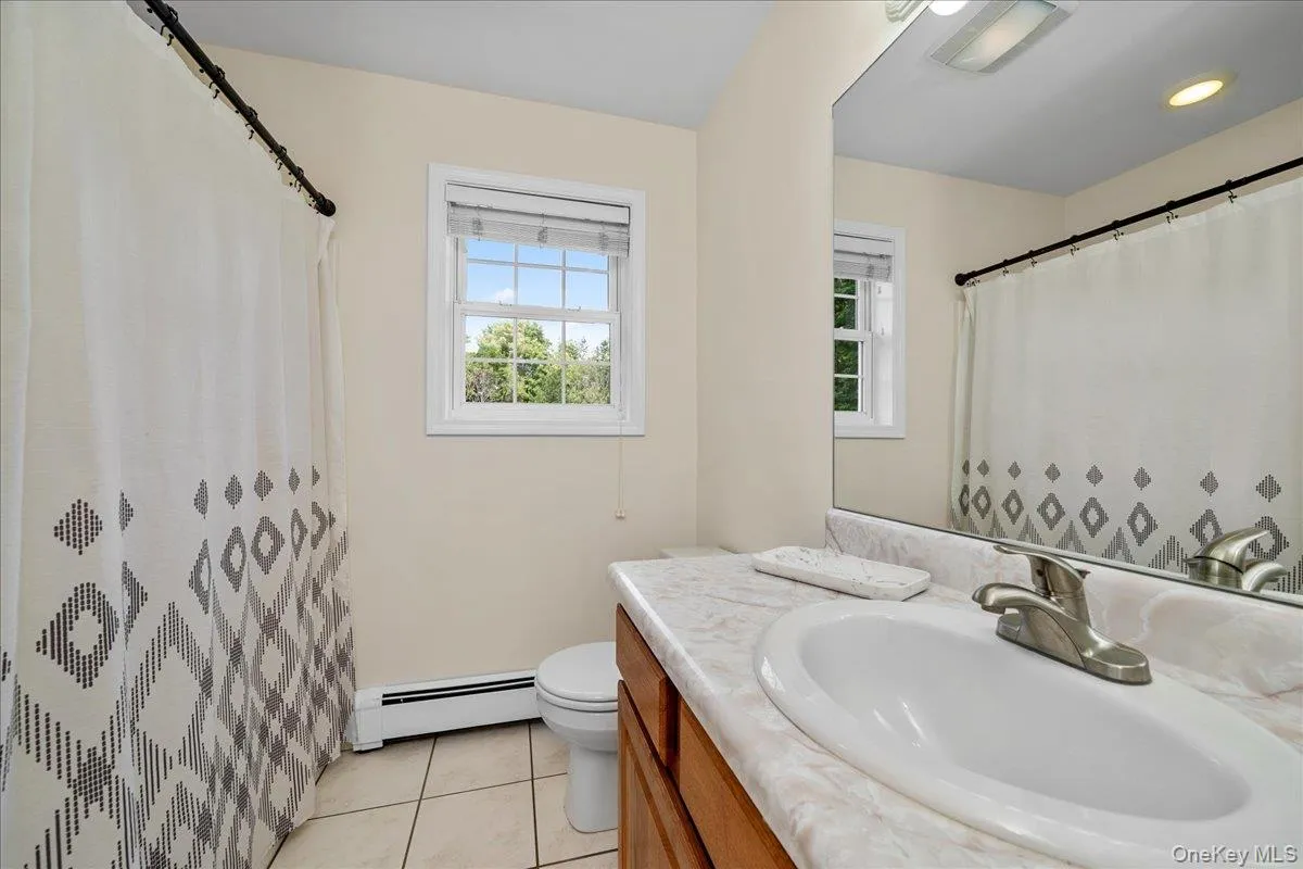Main Bathroom featuring a window, tile flooring, vanity with an integrated sink, full-width mirror, and a toilet Main Bathroom featuring a window, tile flooring, vanity with an integrated sink, full-width mirror, and a toilet