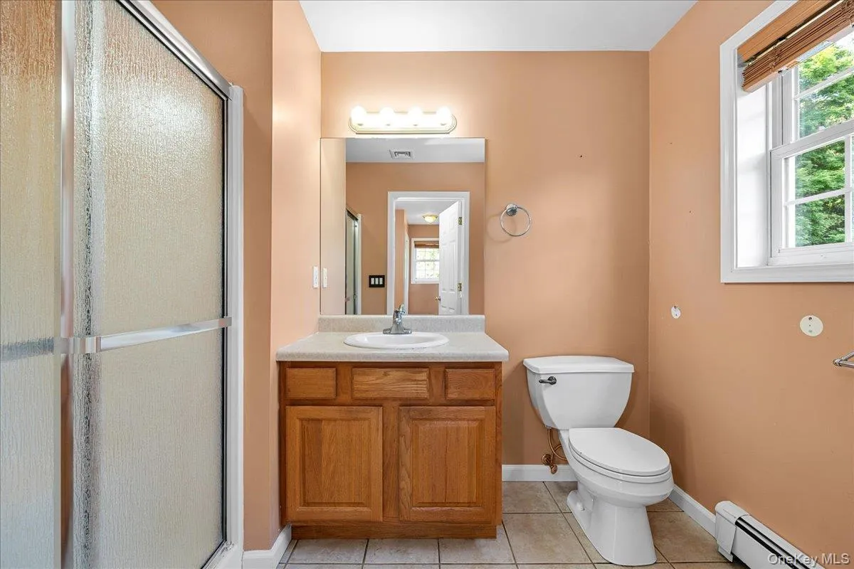 Primary Bathroom featuring a wood vanity with integrated sink, a frameless mirror with vanity lighting, and a white toilet Primary Bathroom featuring a wood vanity with integrated sink, a frameless mirror with vanity lighting, and a white toilet