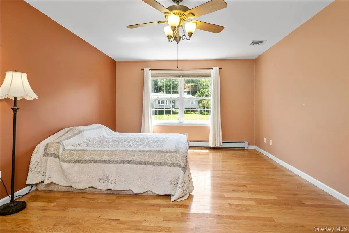 Spacious room featuring wood-finish flooring, a ceiling fan with integrated lighting, and a window with white trim. Spacious room featuring wood-finish flooring, a ceiling fan with integrated lighting, and a window with white trim.