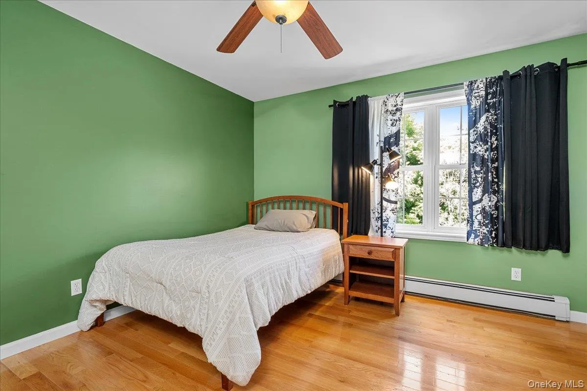 bedroom featuring wood-finish flooring, a ceiling fan with light fixture, and a window with white trim bedroom featuring wood-finish flooring, a ceiling fan with light fixture, and a window with white trim