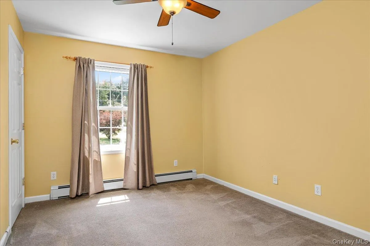 Carpeted bedroom with a ceiling fan light fixture, double-hung window, and baseboard heating Carpeted bedroom with a ceiling fan light fixture, double-hung window, and baseboard heating