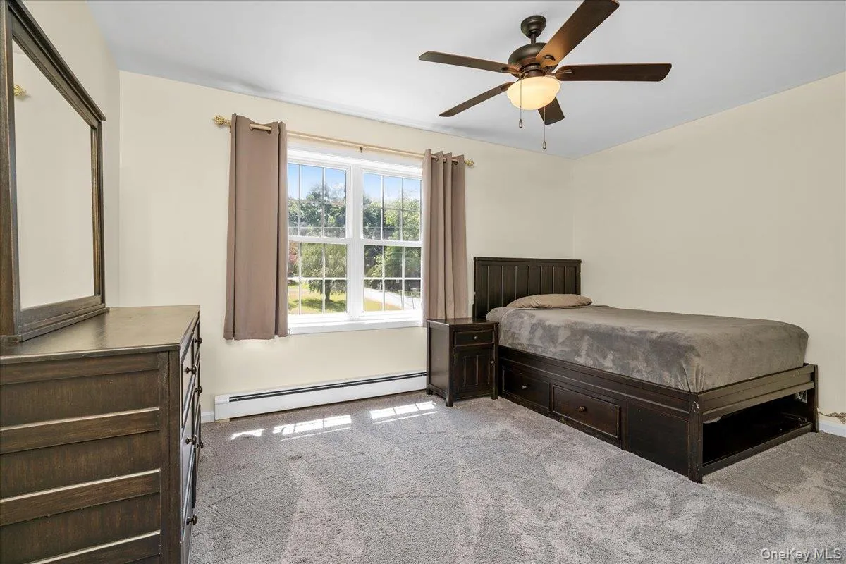 Carpeted bedroom featuring a ceiling fan with integrated lighting, a large window with white muntins, and neutral-toned walls Carpeted bedroom featuring a ceiling fan with integrated lighting, a large window with white muntins, and neutral-toned walls