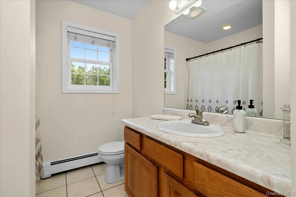 Main Bathroom featuring a wood vanity with an integrated sink, a large wall-mounted mirror, and a window with blinds Main Bathroom featuring a wood vanity with an integrated sink, a large wall-mounted mirror, and a window with blinds