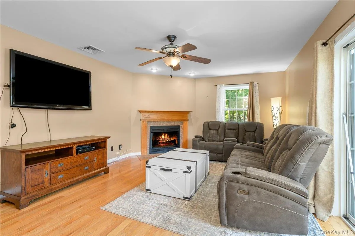 Living room featuring wood-finish flooring, a fireplace with a wood mantle, and a ceiling fan with integrated lighting. Living room featuring wood-finish flooring, a fireplace with a wood mantle, and a ceiling fan with integrated lighting.