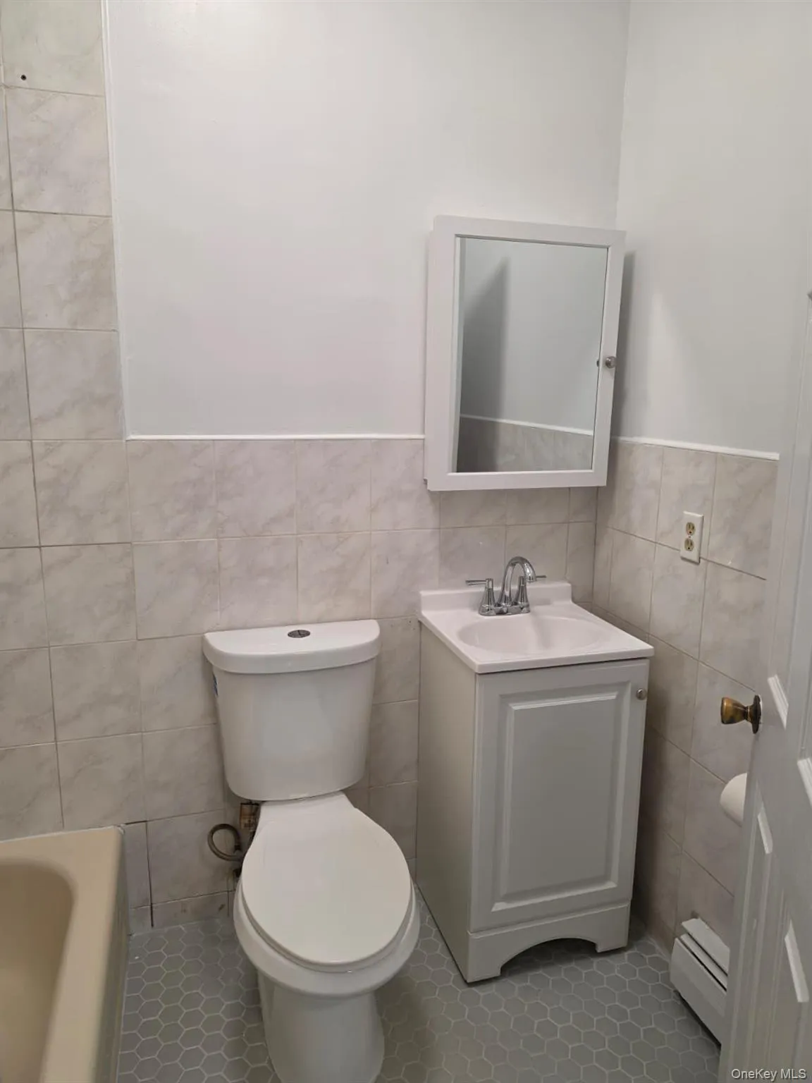 Bathroom featuring floor-to-ceiling tiling, a white vanity with a ceramic sink, a mirrored medicine cabinet, and hexagonal floor tiles Bathroom featuring floor-to-ceiling tiling, a white vanity with a ceramic sink, a mirrored medicine cabinet, and hexagonal floor tiles