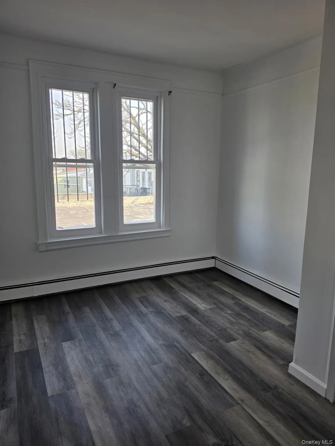 Interior room featuring wood-finish flooring, white painted walls, and two double-hung windows with security bars Interior room featuring wood-finish flooring, white painted walls, and two double-hung windows with security bars