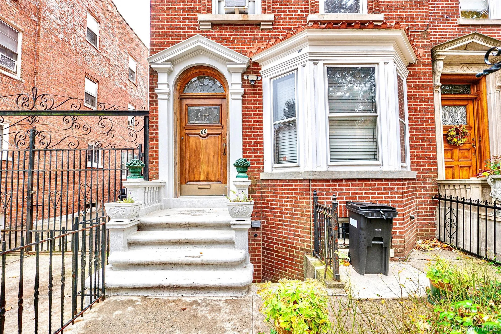 Brick facade with a bay window and arched wooden entry door featuring decorative glass Brick facade with a bay window and arched wooden entry door featuring decorative glass